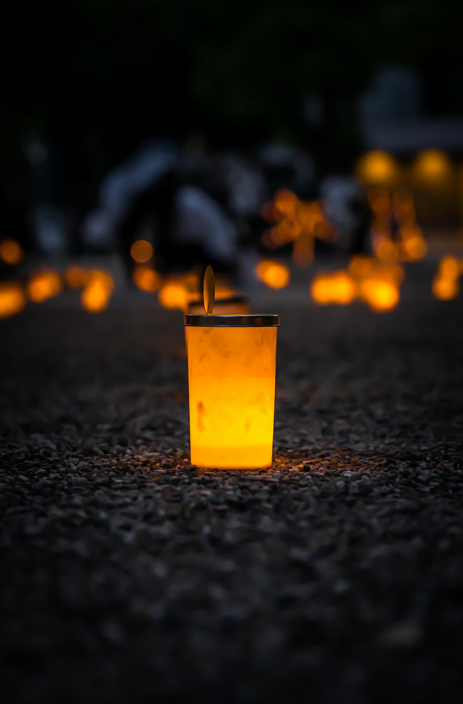 Un vaso transparente que brilla con luz naranja brillante rodeado de luces de velas tenues