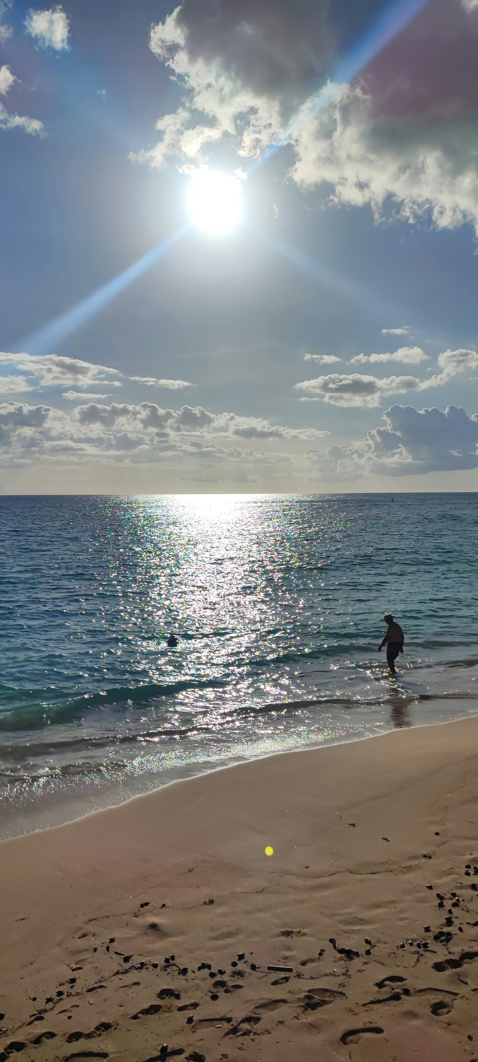 Person wading in blue ocean at sandy beach under bright sun