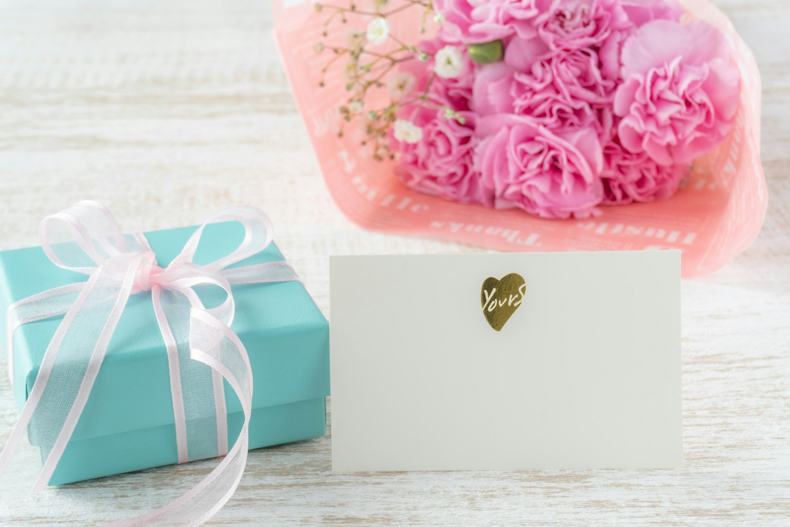 Eine blaue Geschenkbox und ein rosa Blumenstrauß mit einer weißen Karte davor
