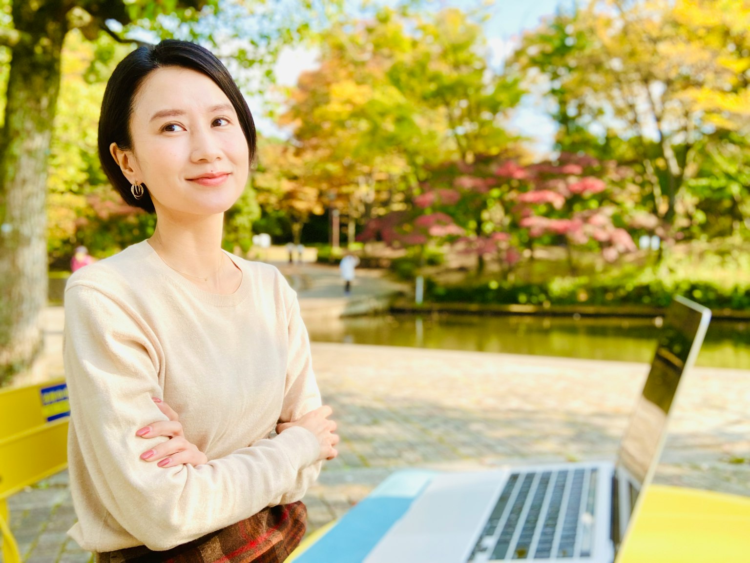 Porträt einer Frau, die in einem Park an einem Laptop arbeitet und inmitten einer schönen Herbstlandschaft lächelt