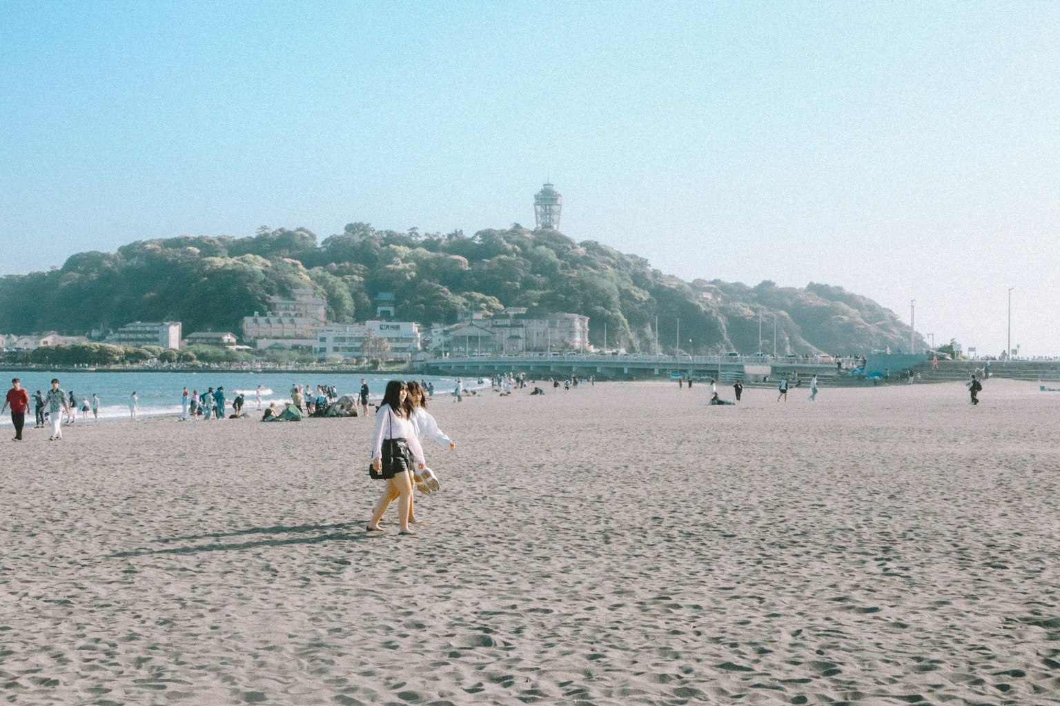 Scena di spiaggia con persone che camminano e un faro sullo sfondo