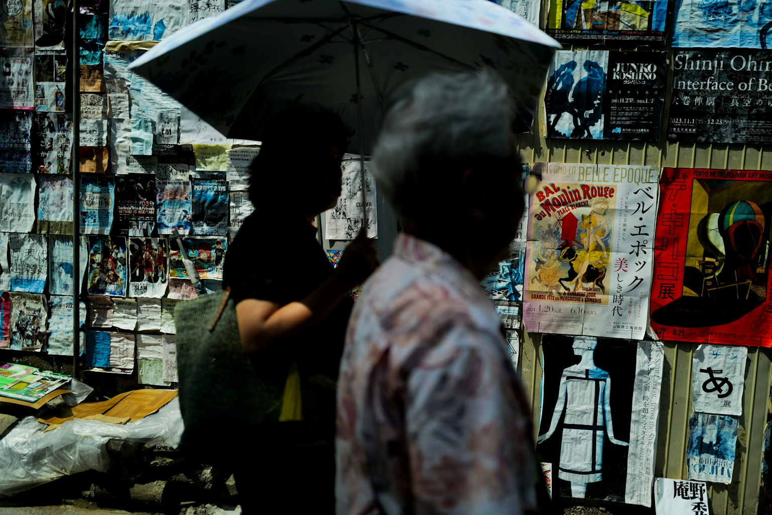 Menschen, die mit Regenschirmen an einer Wand mit Plakaten und Kunst an einer Straßenecke vorbeigehen