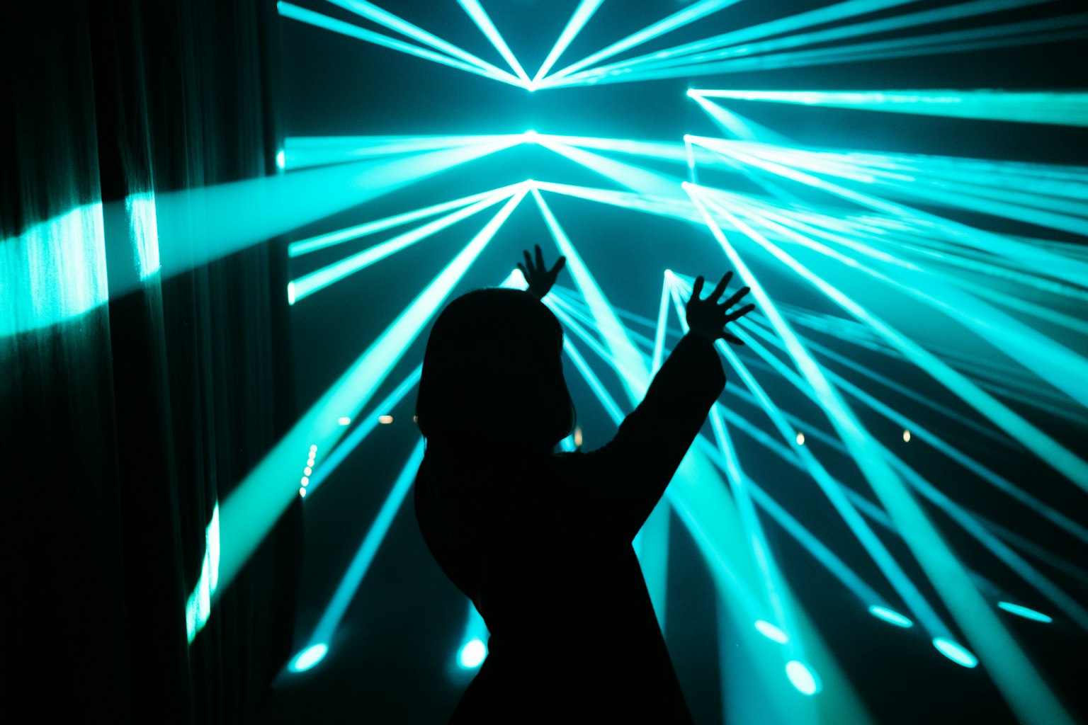 Silhouette einer Person, die die Hände zwischen blauen Laserlichtern hebt