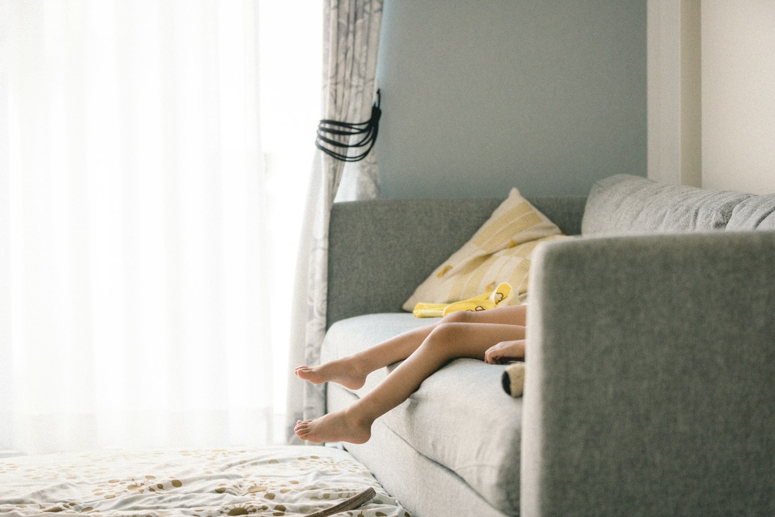 Füße eines Kindes auf einem Sofa nahe einem hellen Fenster mit einem dekorativen Kissen