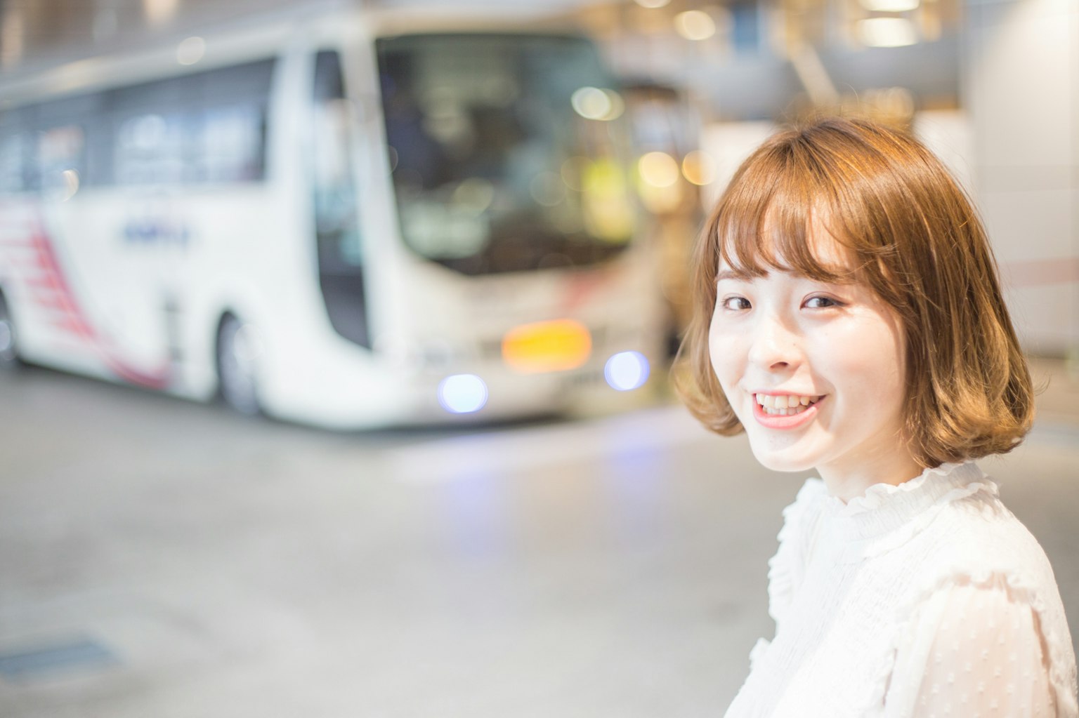 ผู้หญิงยิ้มถ่ายรูปใกล้รถบัสในสภาพแวดล้อมที่สว่าง