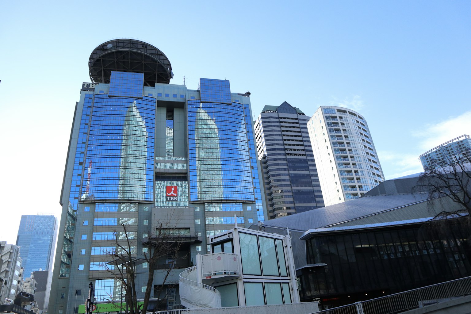 現代摩天大樓，玻璃外觀，周圍是其他建築，背景是晴朗的藍天