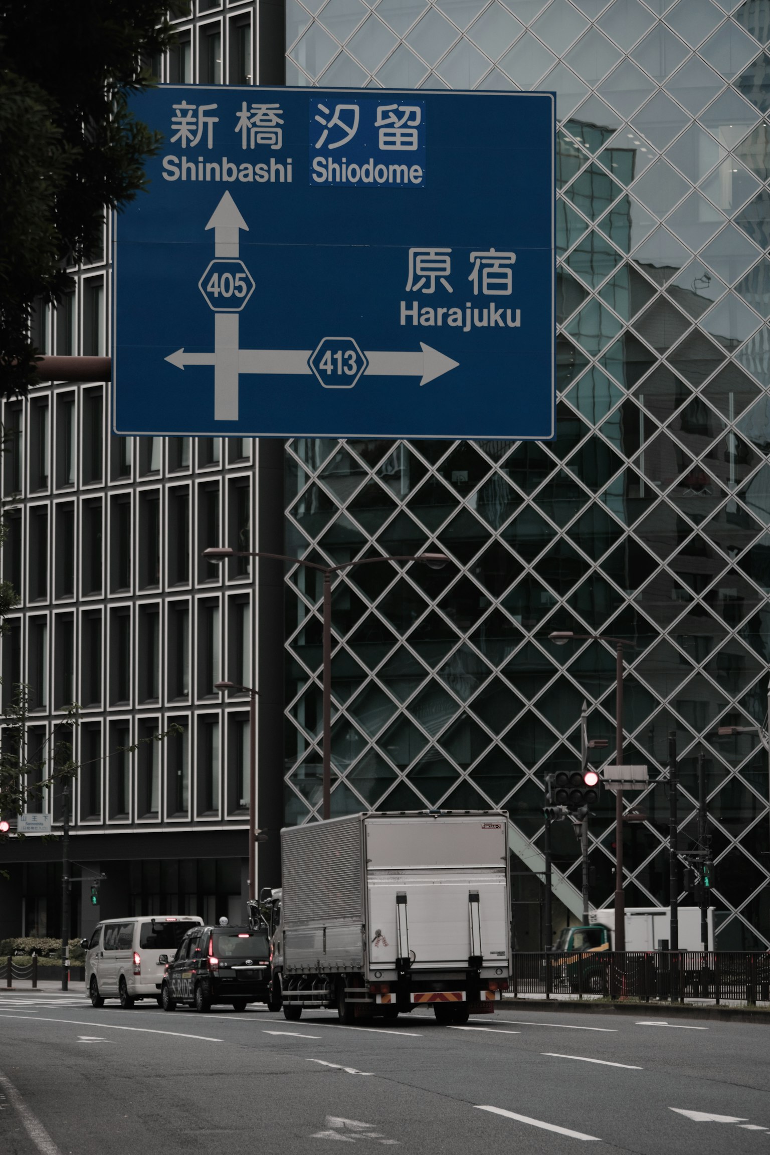 Blue road sign indicating Shinbashi and Harajuku with modern buildings in the background