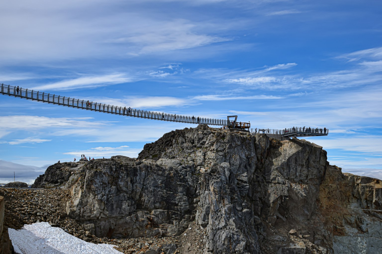 สะพานแขวนเหนือภูมิประเทศหินที่มีหิมะและท้องฟ้าสีฟ้า