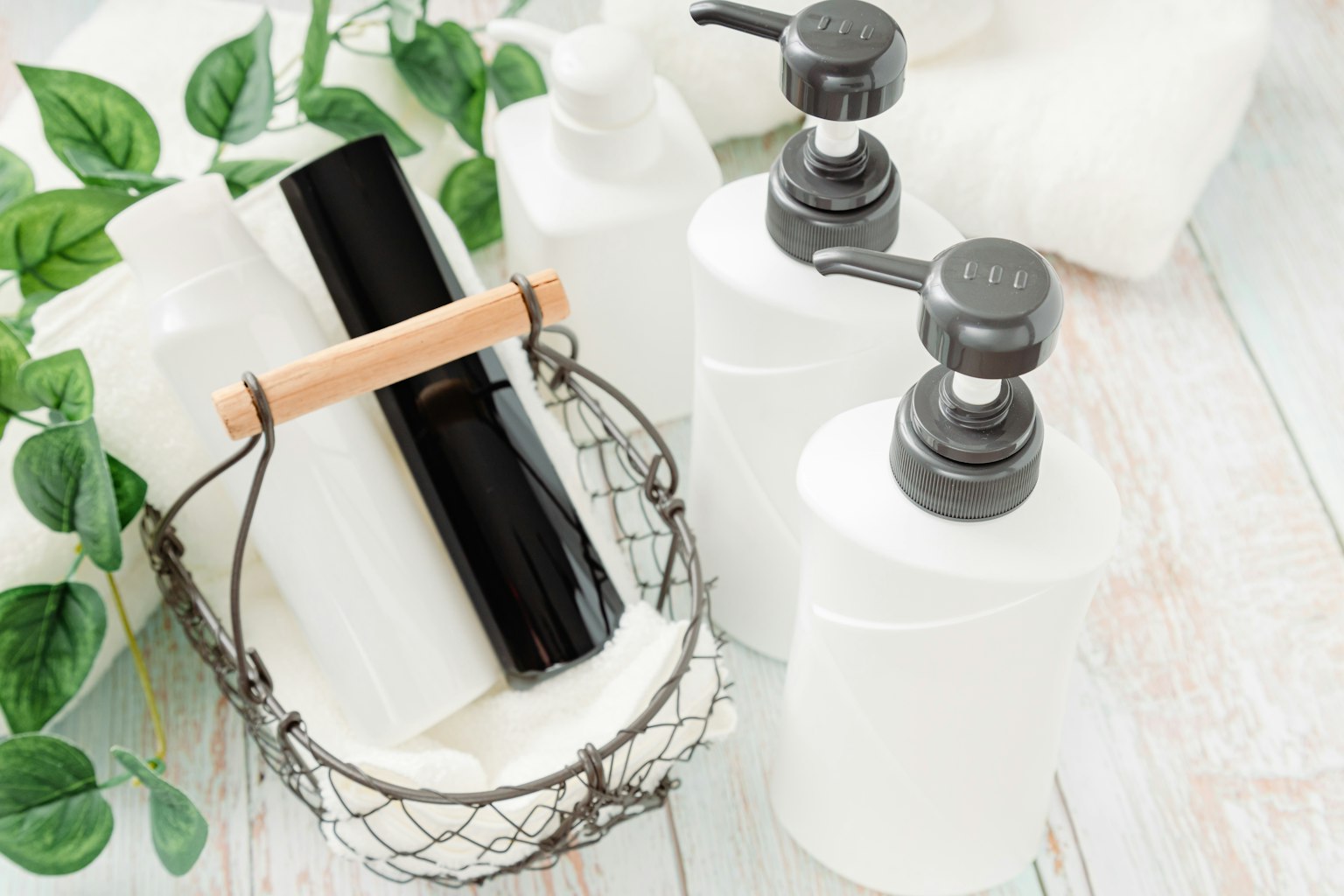 Chai trắng và ống đen trong giỏ cùng với khăn tắm và cây xanh