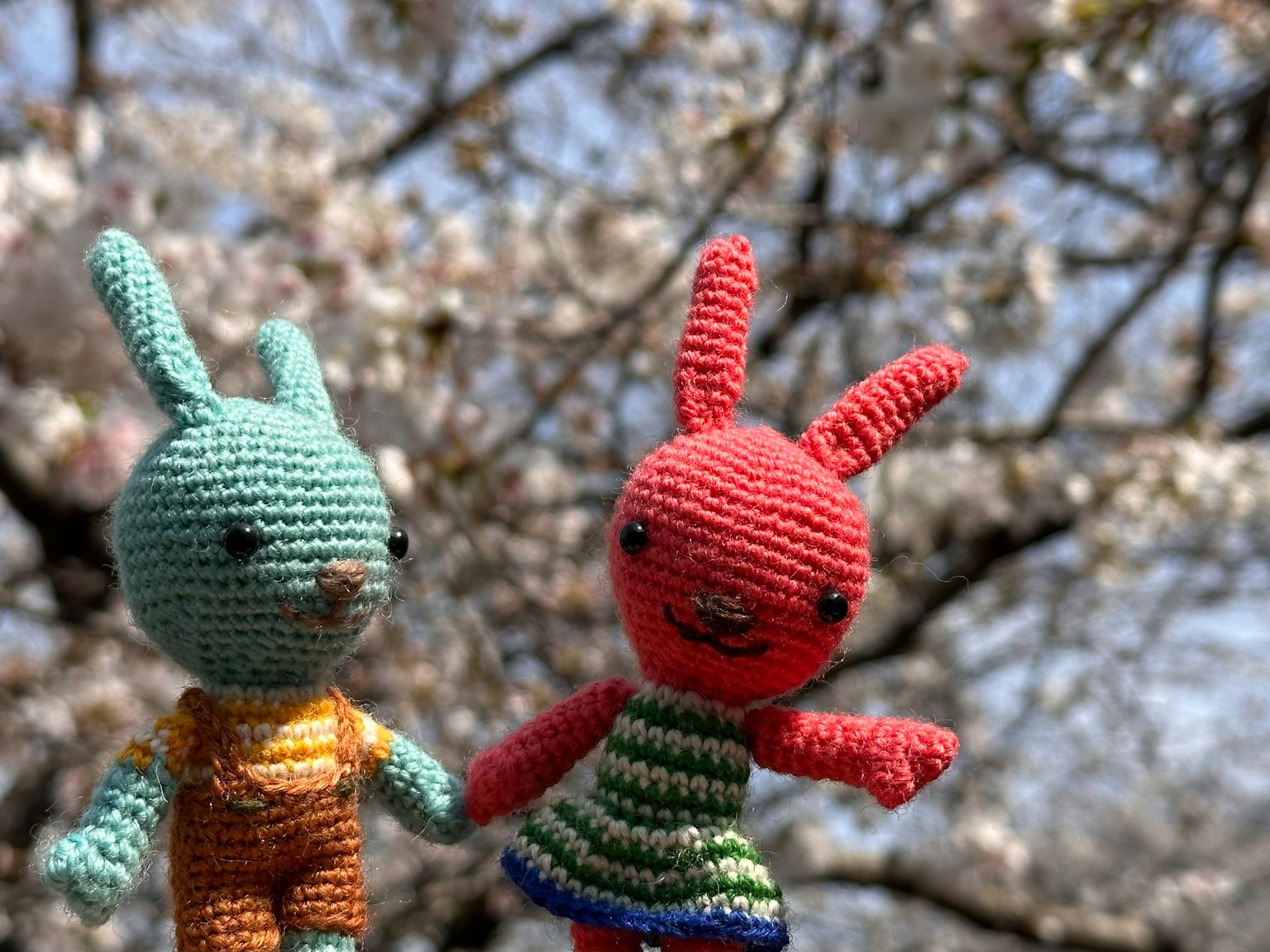 Dos conejitos de ganchillo tomados de la mano bajo un árbol de cerezo en flor