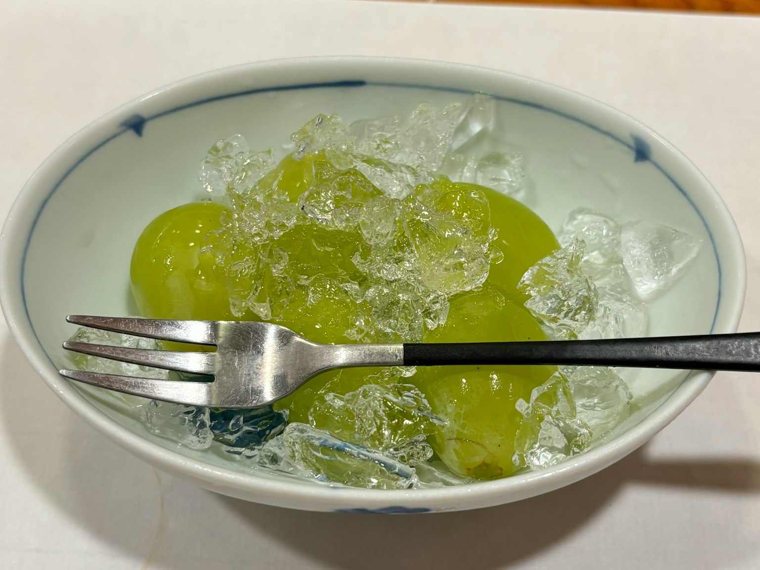 碗中放有绿色水果和冰块，配有叉子