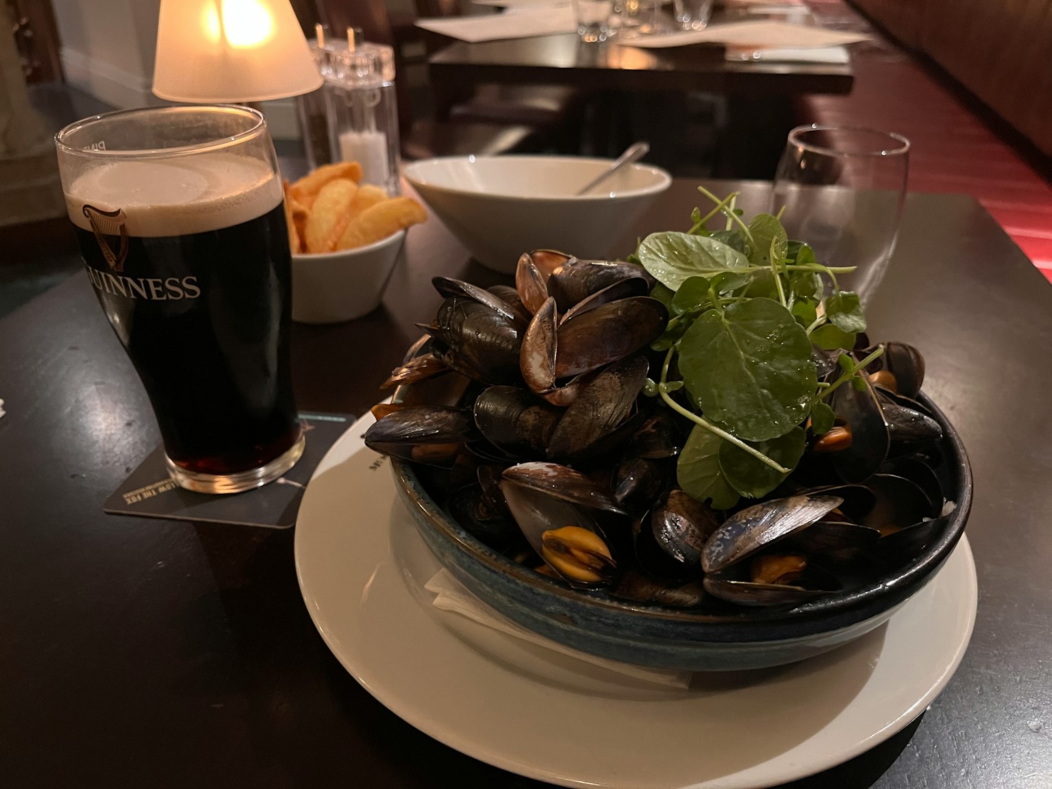 Sebuah gelas bir stout di samping mangkuk kerang yang dihias dengan herba di meja makan