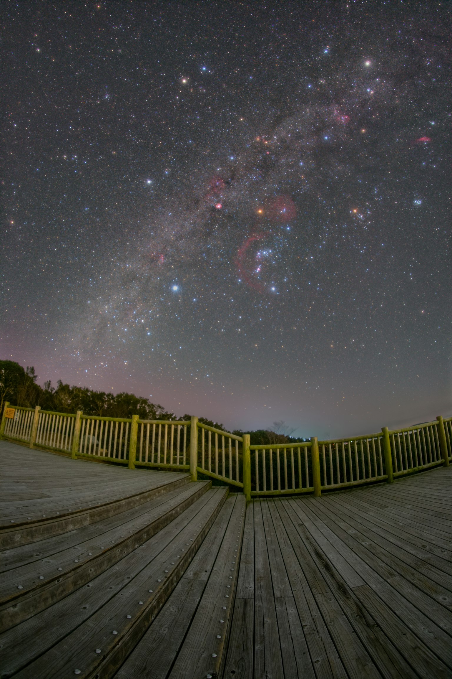 Deck de madera bajo un cielo estrellado con la Vía Láctea y numerosas estrellas