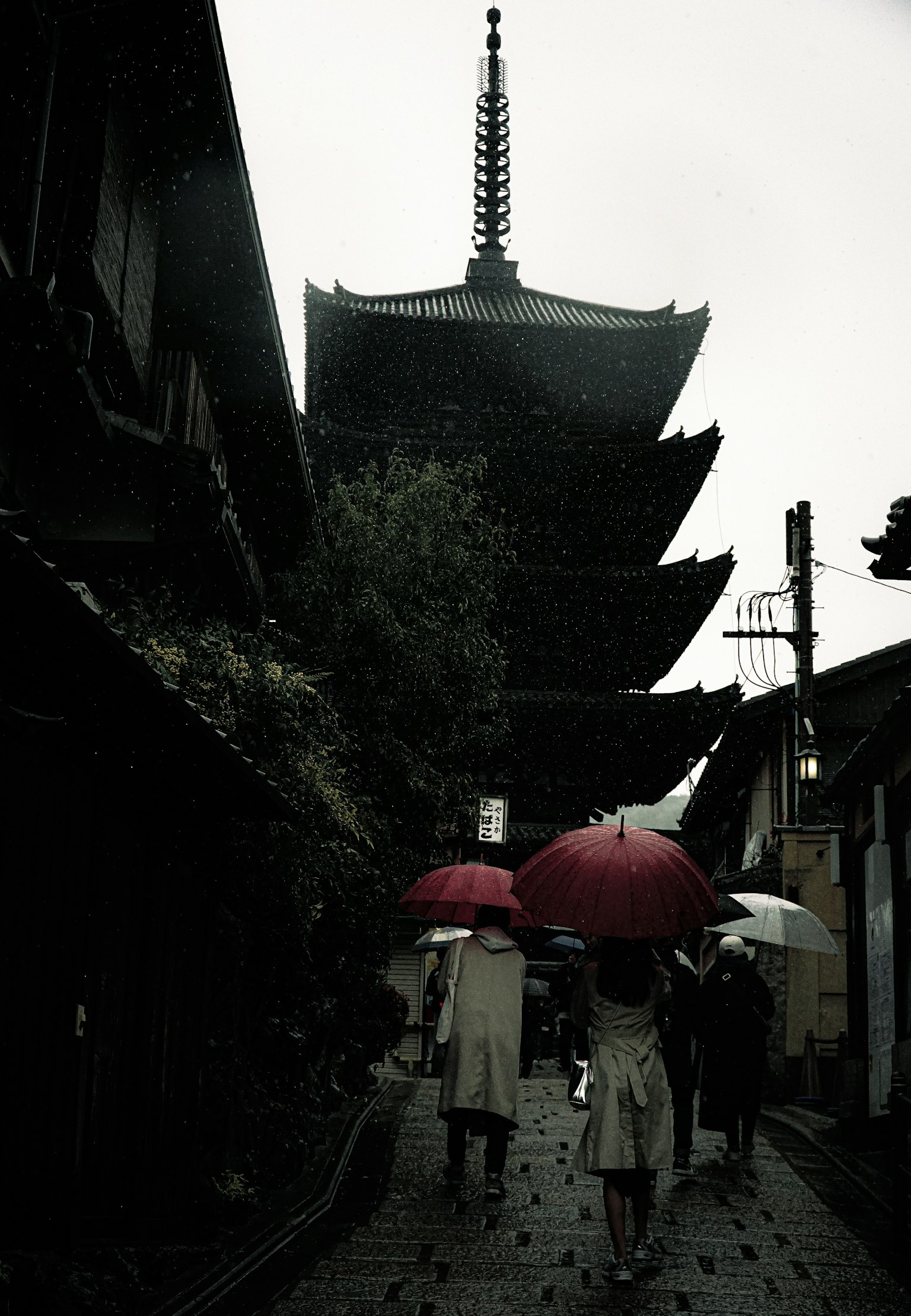 Silhouette of a pagoda with people walking under umbrellas in the rain