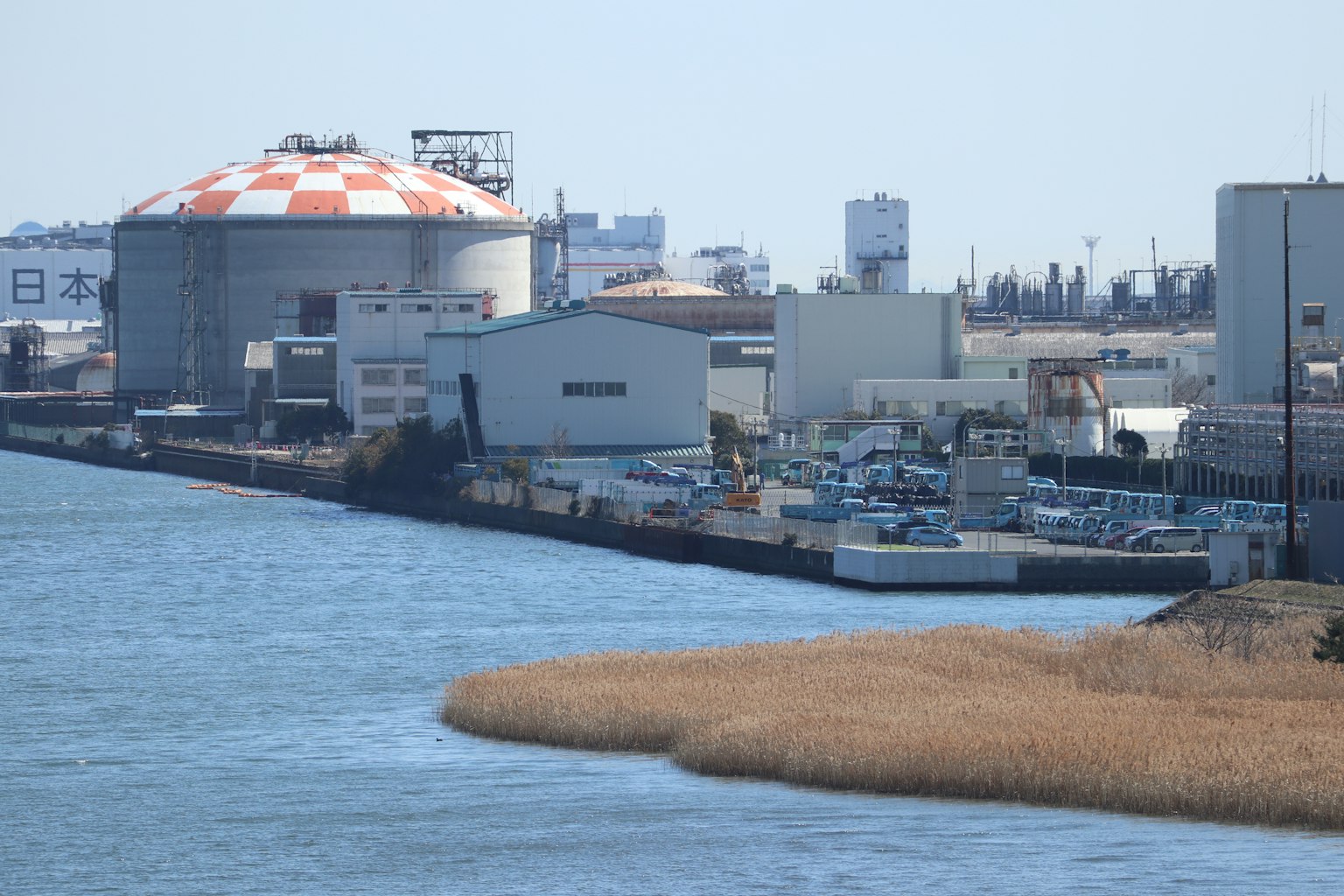 Paesaggio industriale lungo un fiume con un serbatoio rosso e bianco magazzini e prati