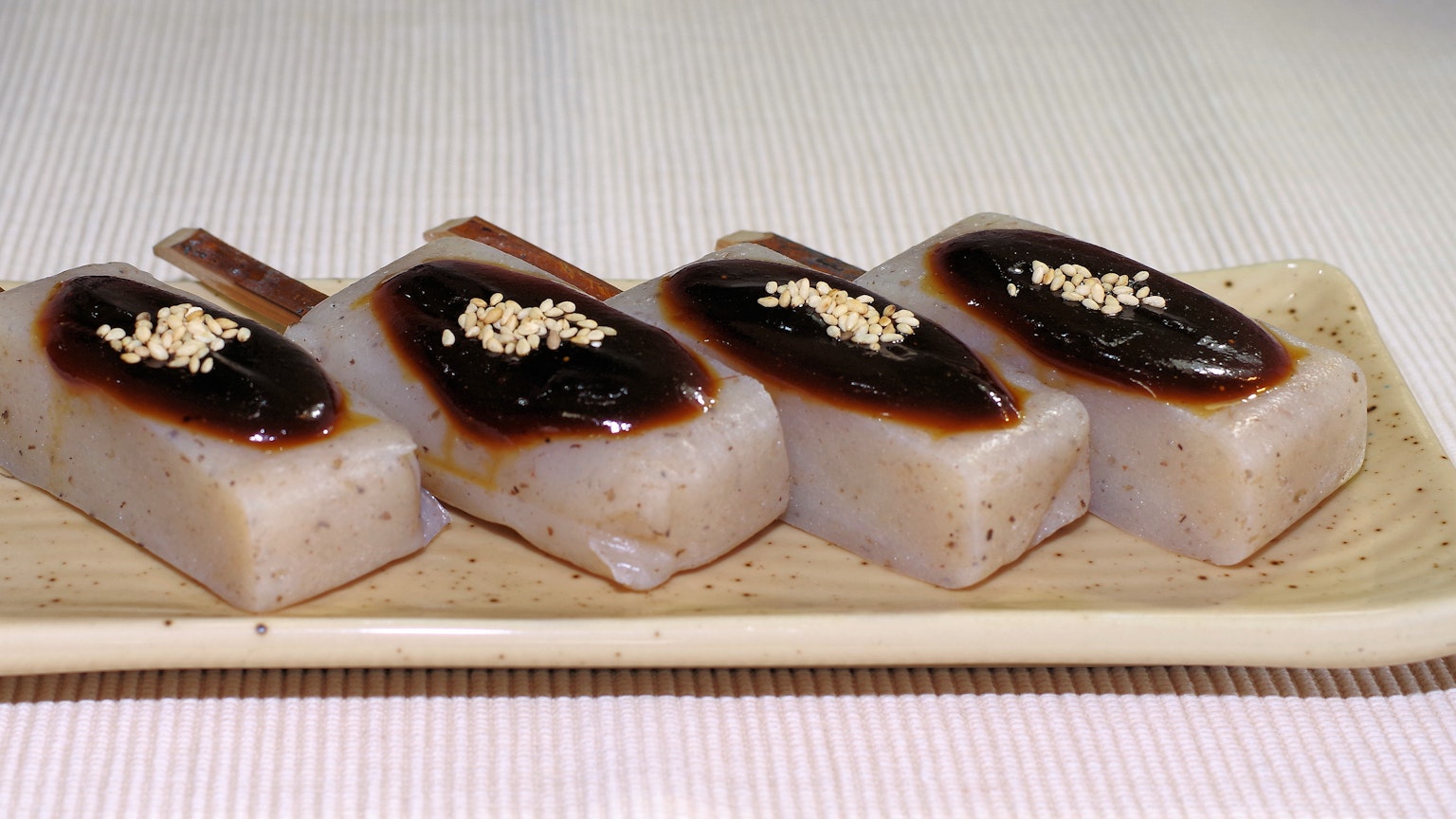 Vier rechteckige japanische Süßigkeiten mit dunkler süßer Sauce und weißen Sesamsamen