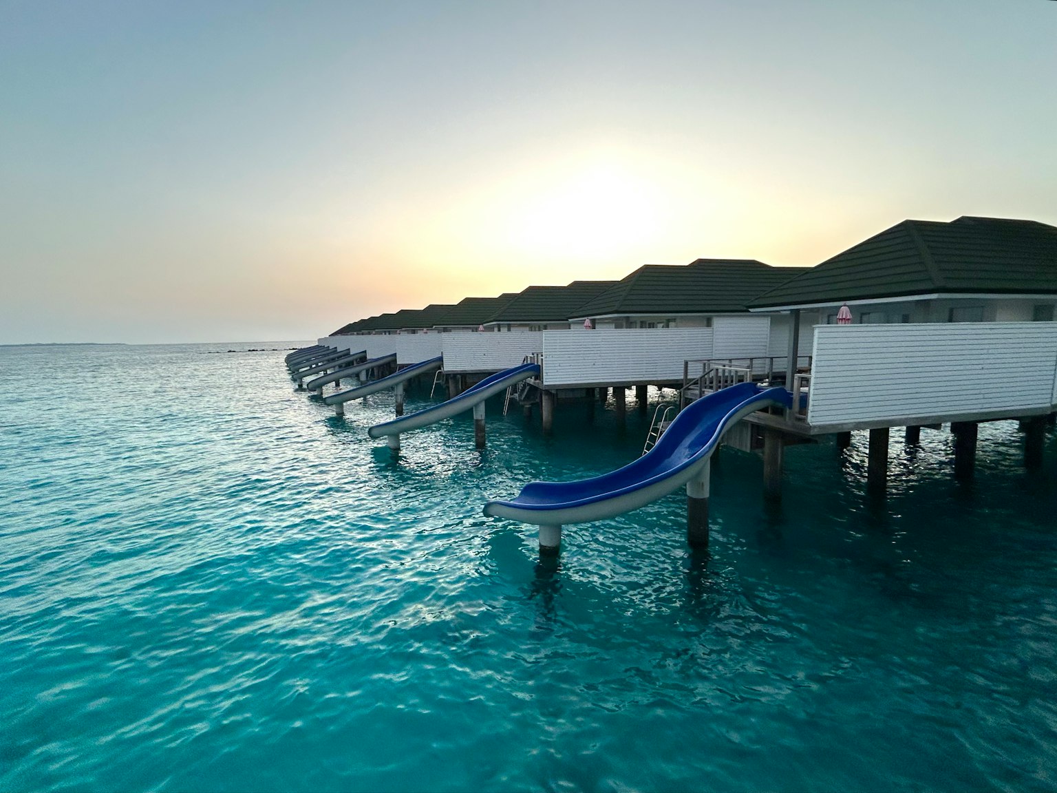 Bungalow sull'acqua con uno scivolo sopra l'acqua turchese al tramonto