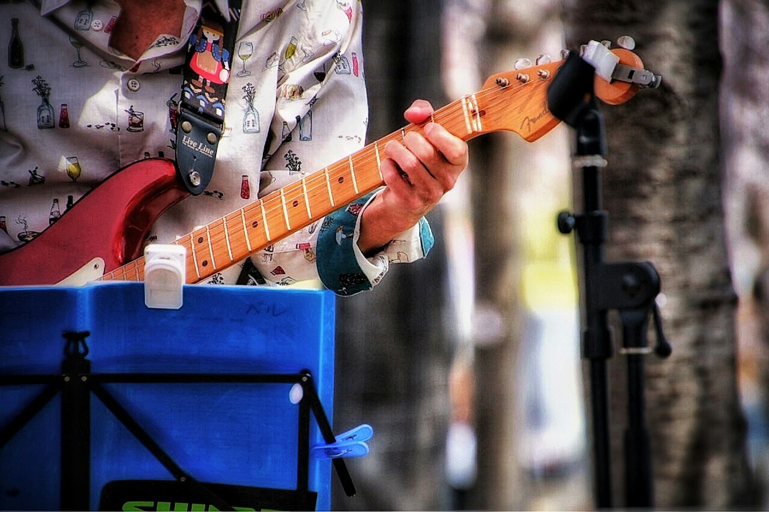 Primer plano de la mano de un hombre tocando una guitarra eléctrica roja con un atril azul