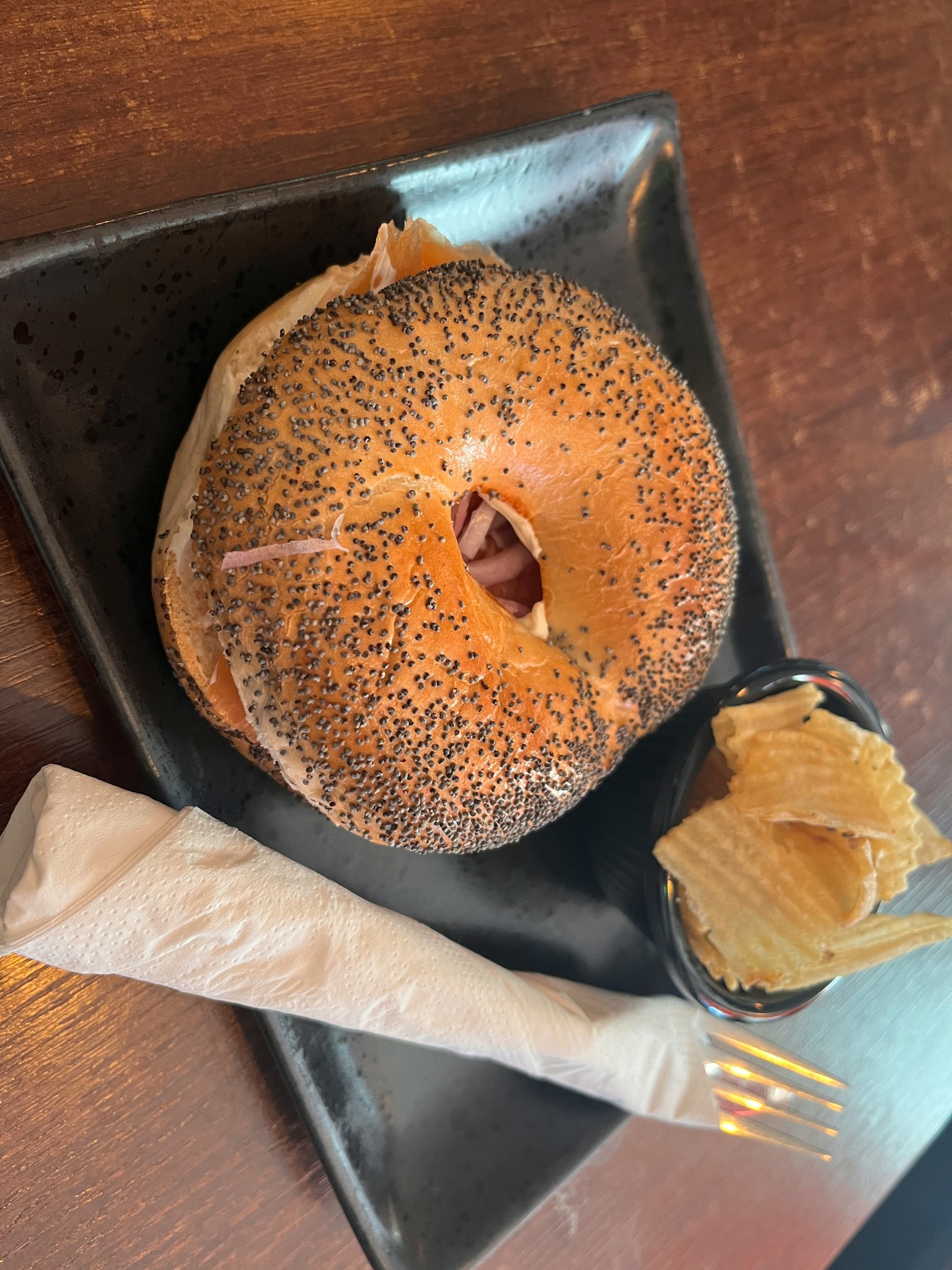 Mohnbrötchen mit Kartoffelchips auf einem schwarzen Teller serviert