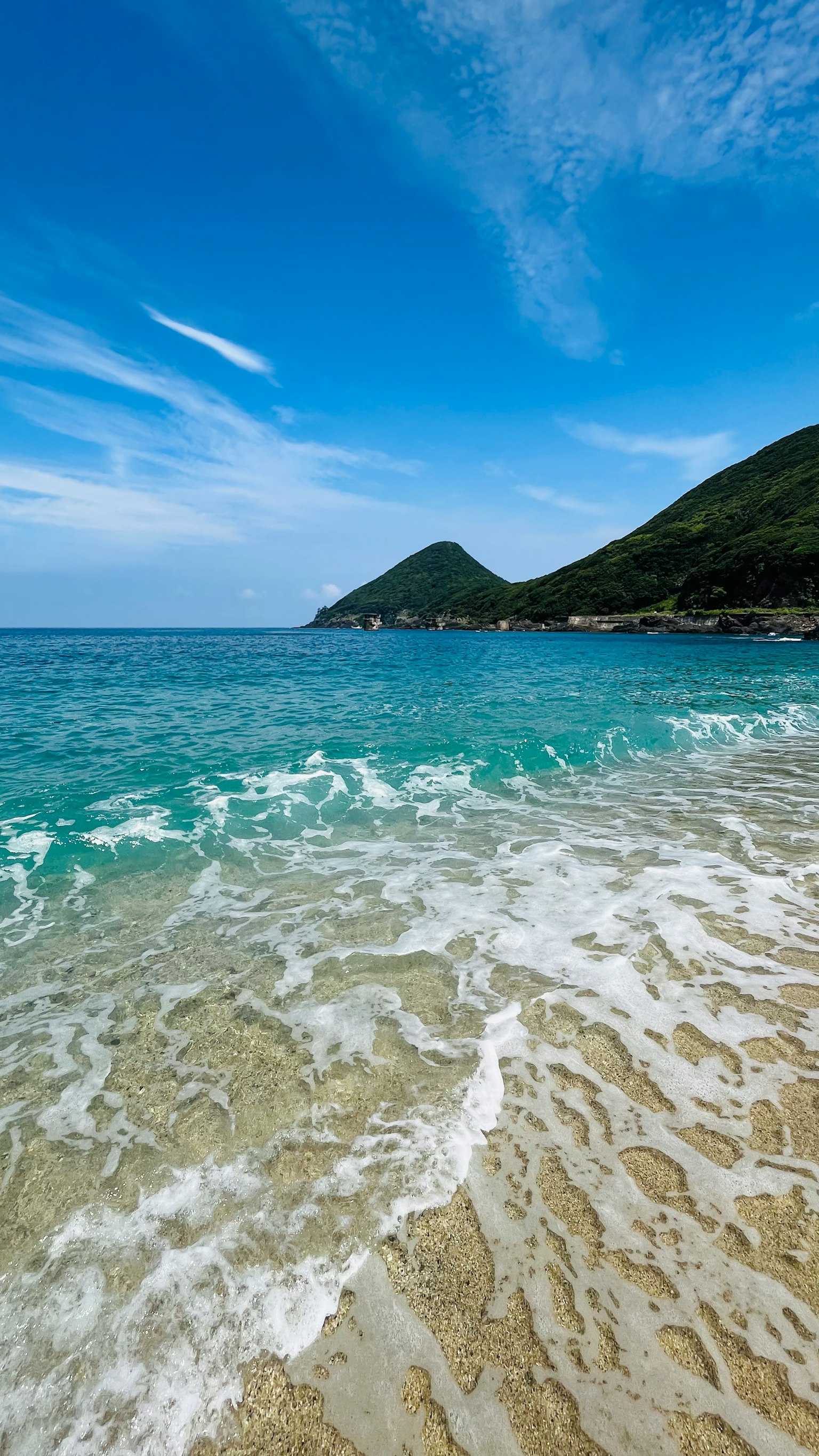 美麗的海灘景色，清澈的碧綠色海水和遠處的綠色山丘