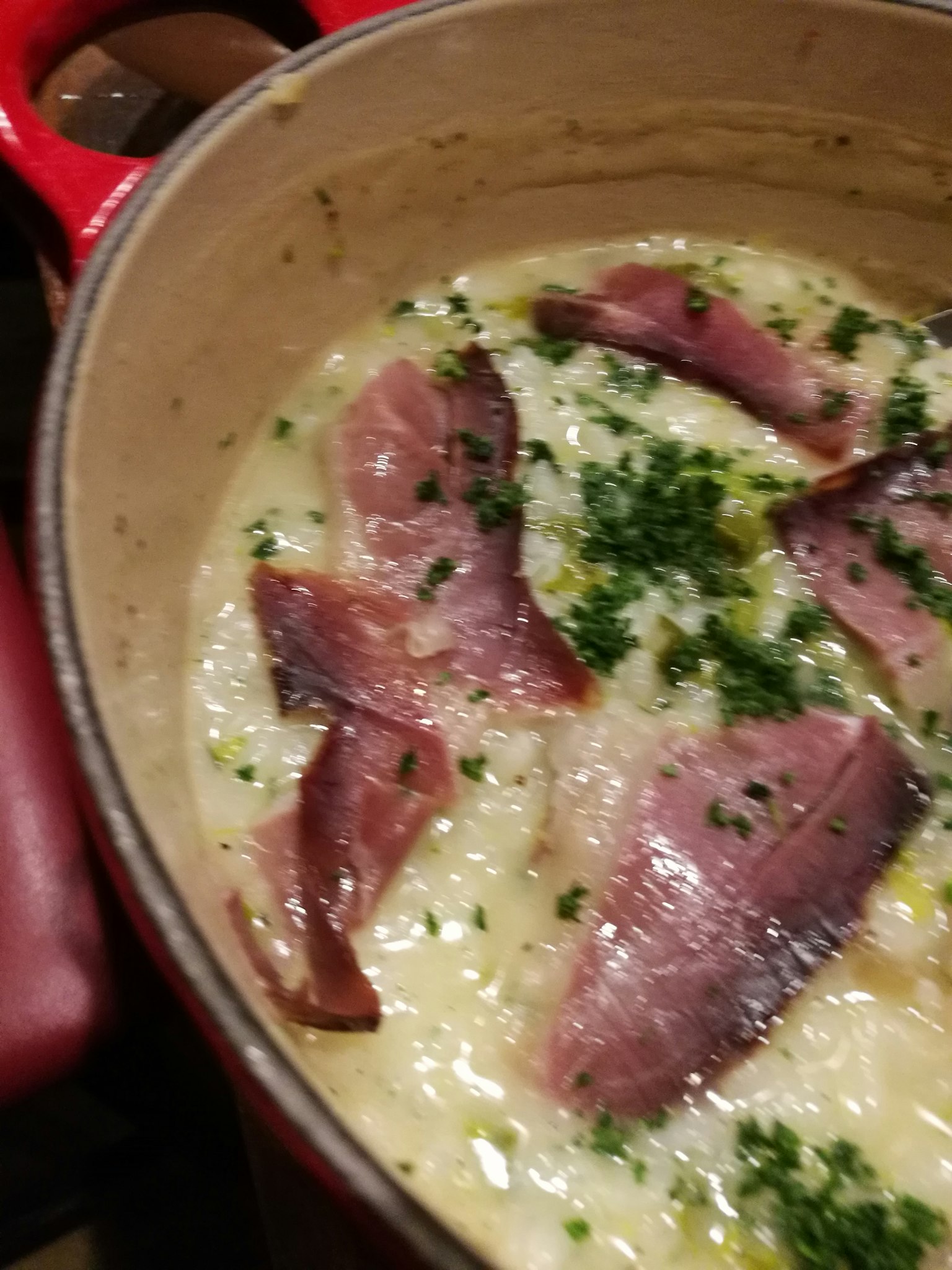 Risotto kem béo phủ với thịt xông khói thái lát và rau mùi trong nồi