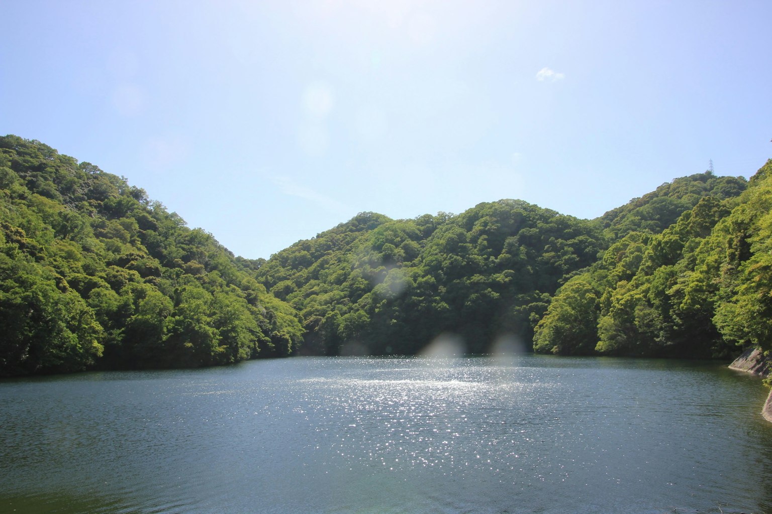 Lago sereno rodeado de colinas verdes bajo un cielo azul claro