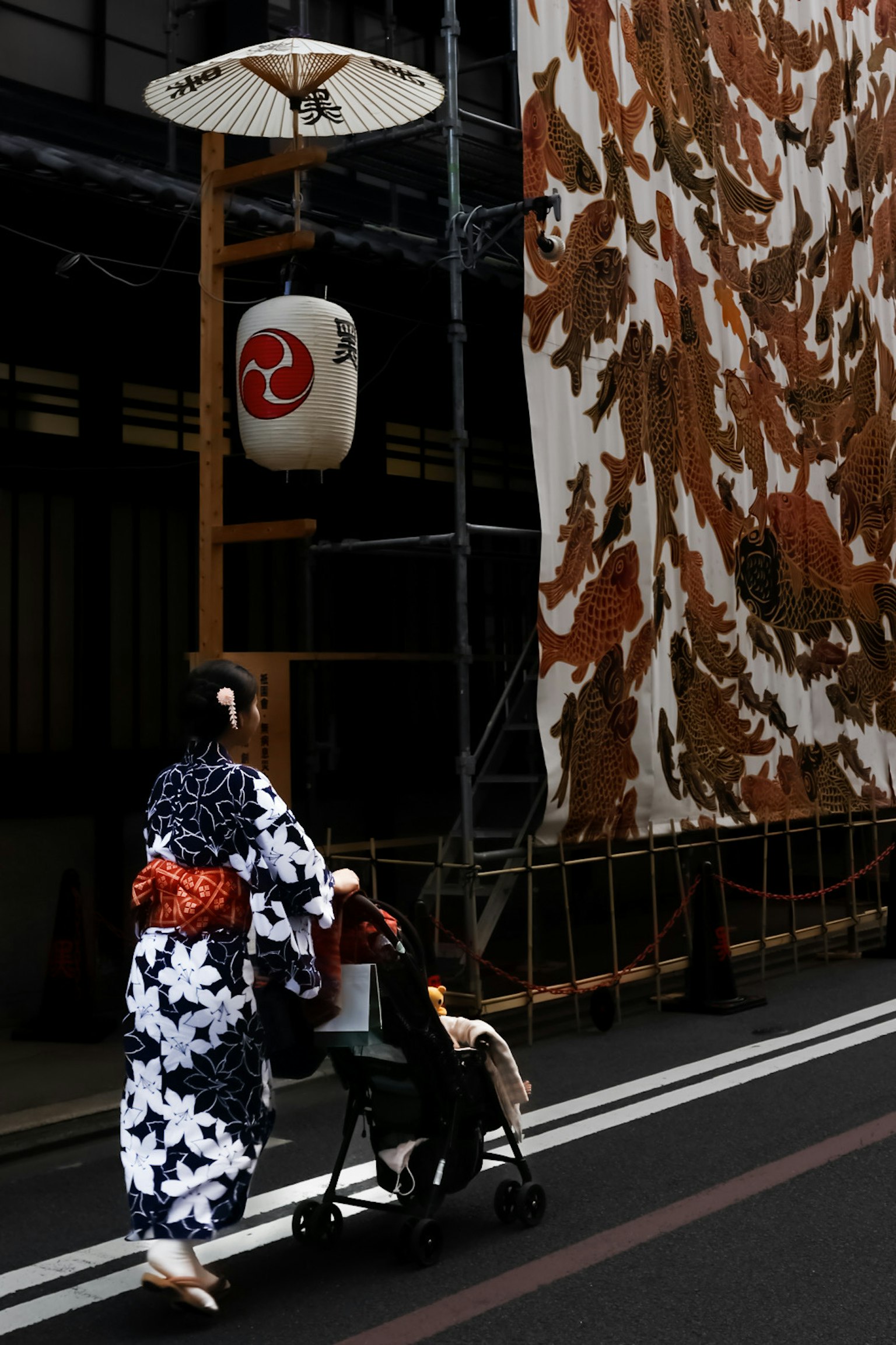 Seorang wanita berpakaian kimono berjalan dengan anak di kereta dorong di latar belakang dekorasi Jepang tradisional