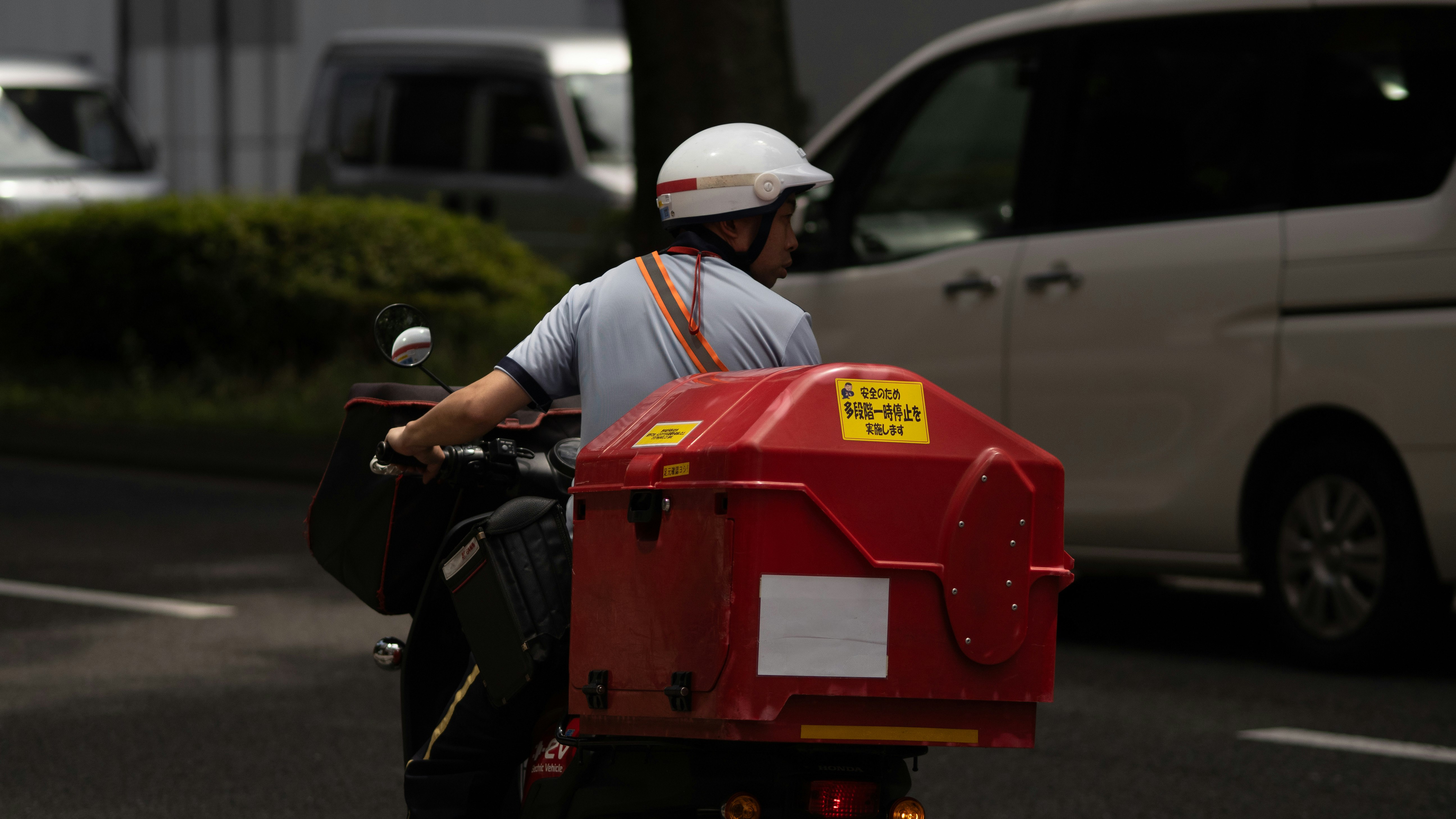 路上で配達用の赤いポスト型バッグを持つ作業員