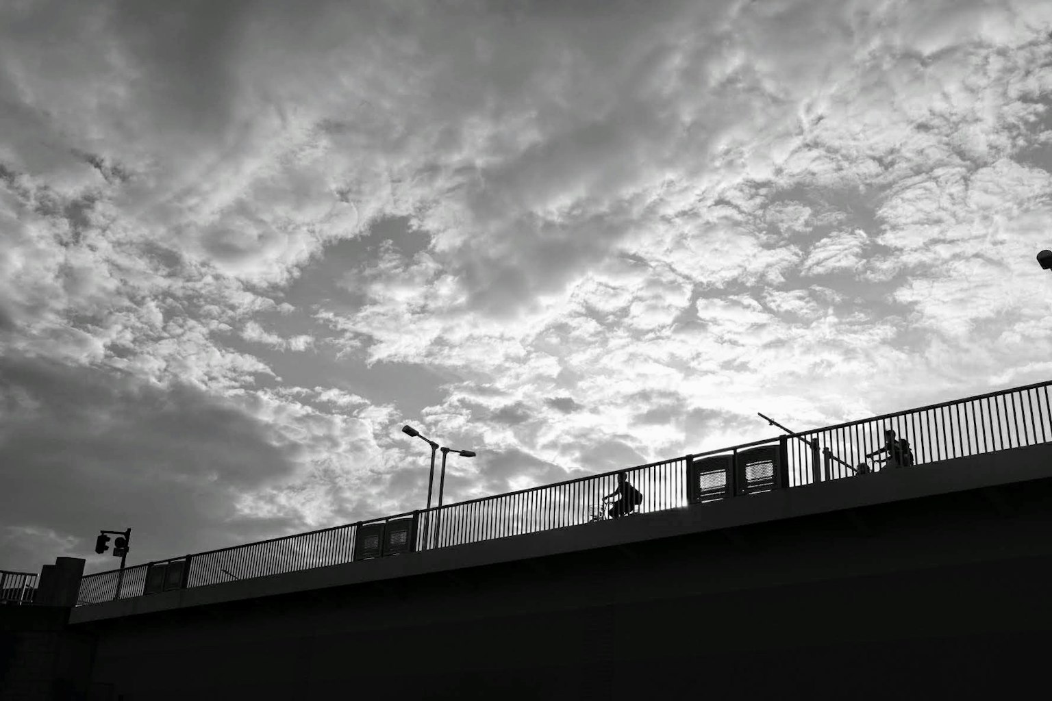 Silhouetten von Personen, die auf einer Brücke gegen einen dramatischen, bewölkten Himmel gehen