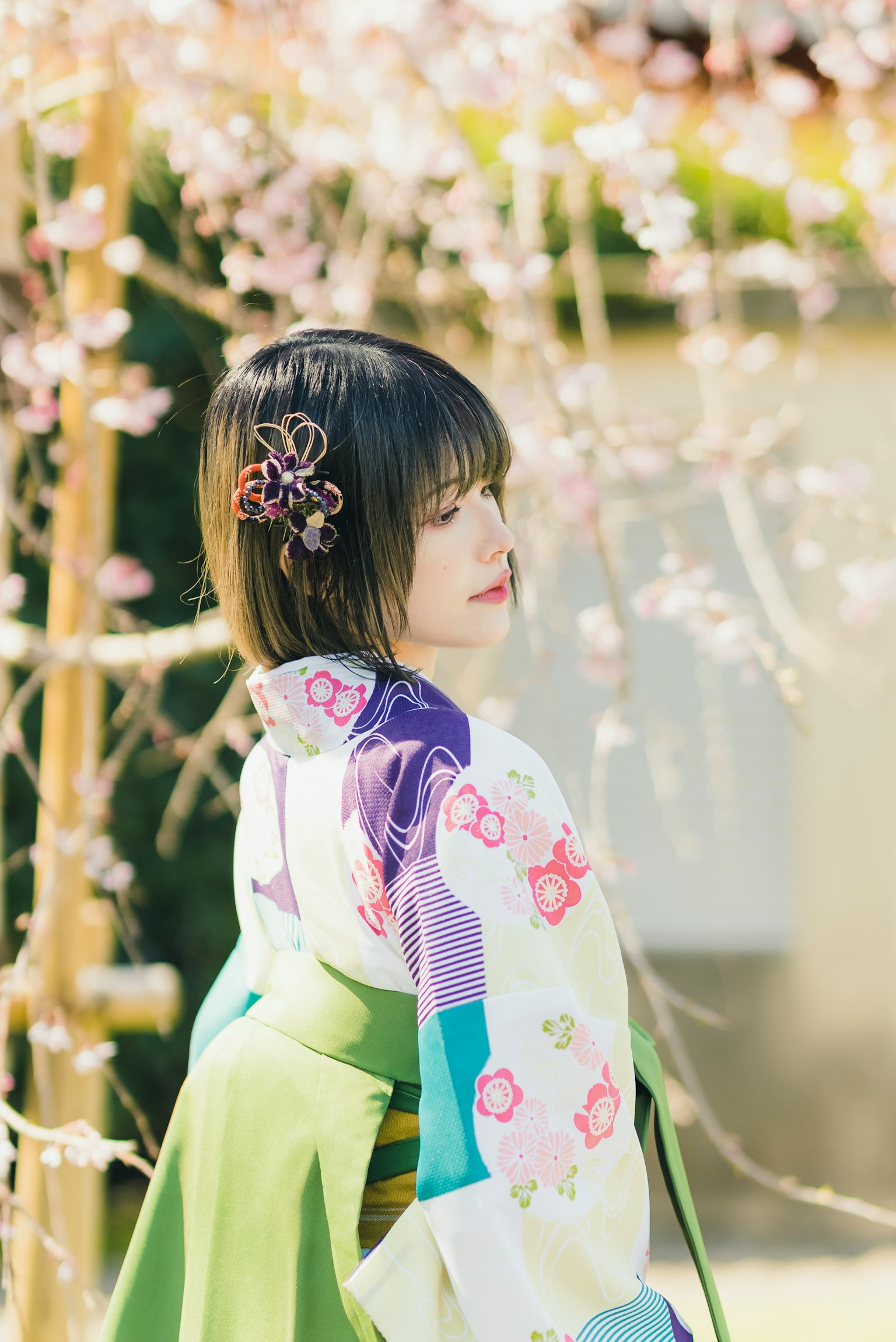 หญิงสาวในกิโมโนสีสันสดใสยืนอยู่ข้างต้นซากุระ