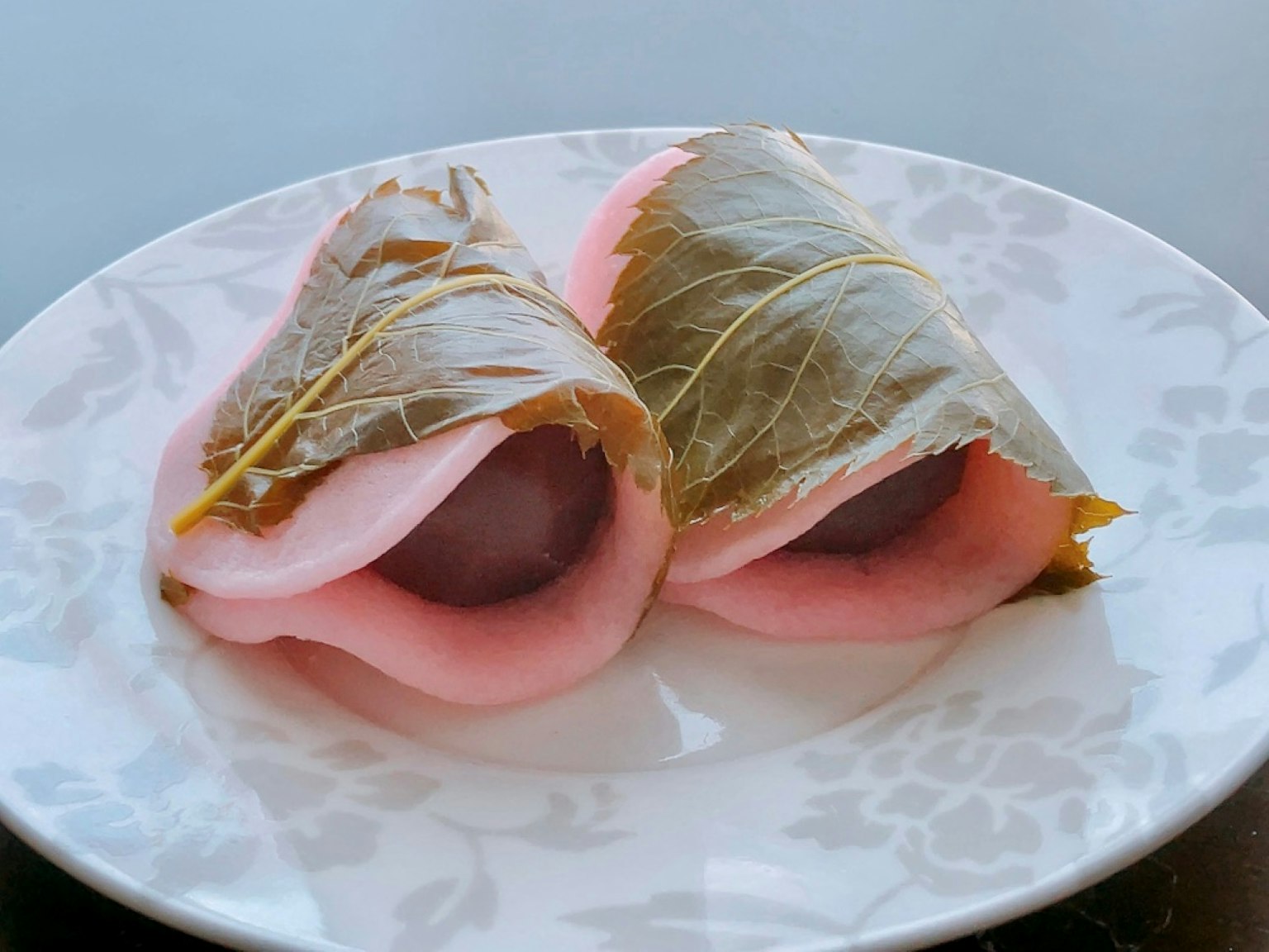 Dos piezas de dulces japoneses tradicionales envueltas en hojas de cerezo en un plato blanco