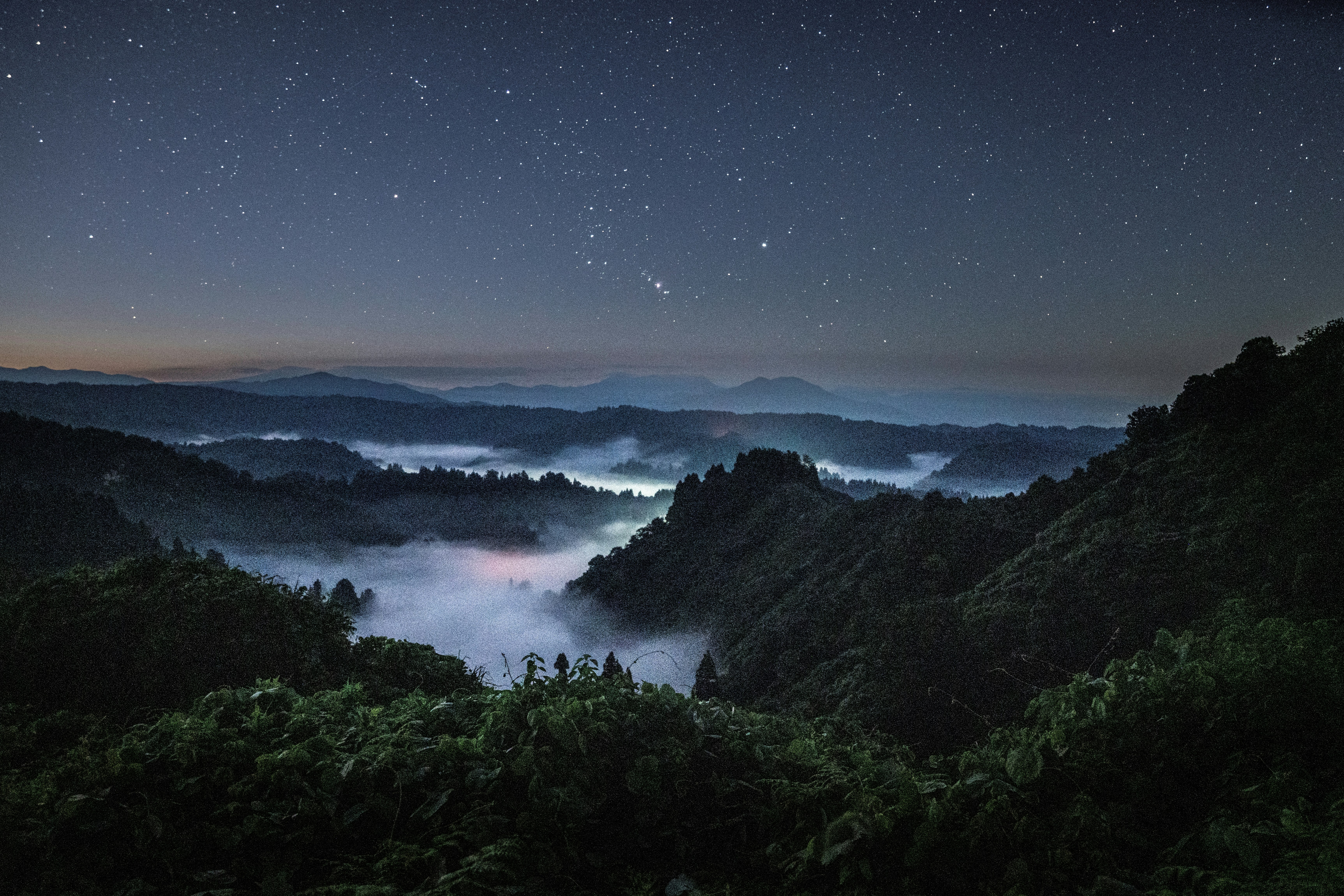 霧に包まれた山並みと星空の夜景