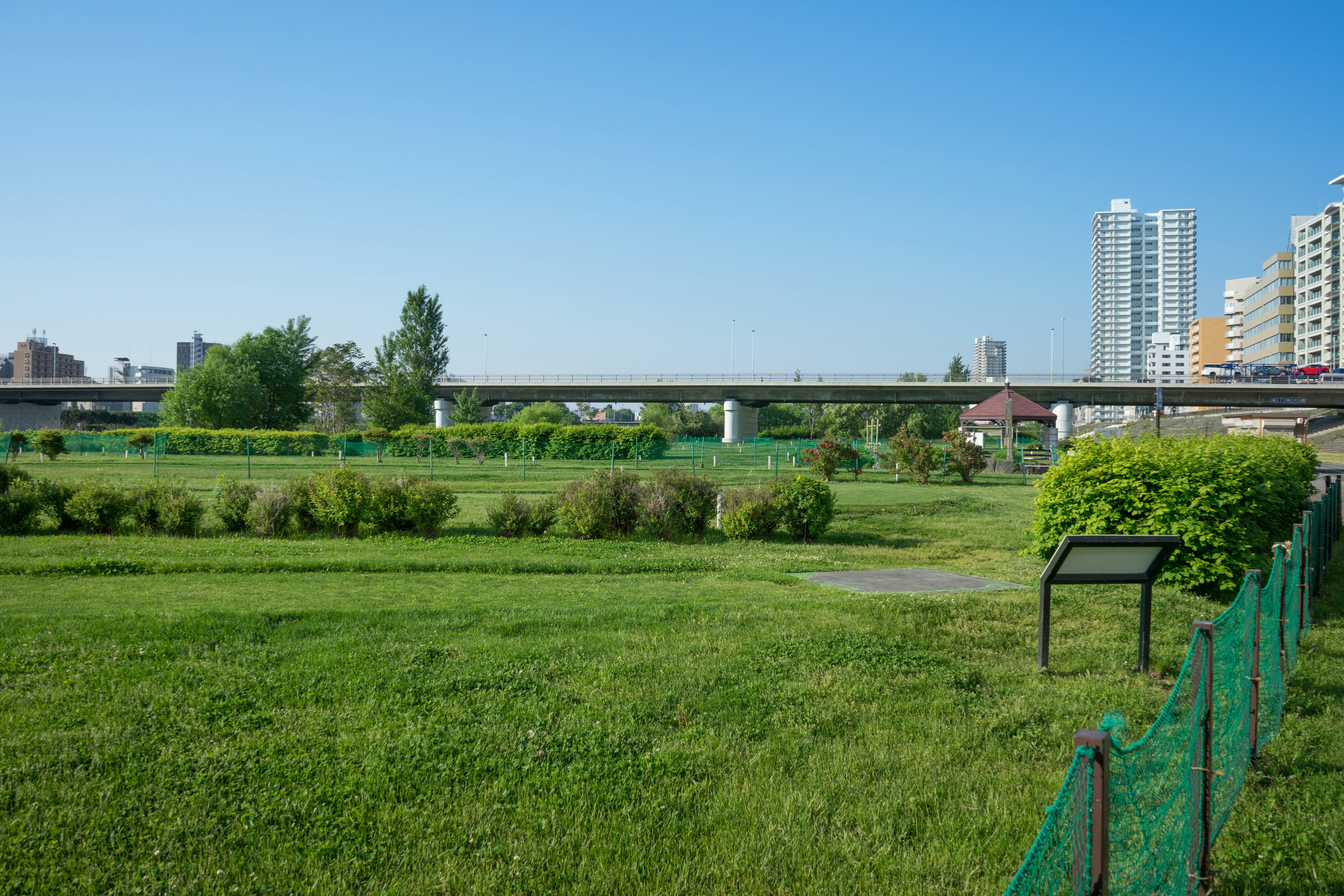 緑の芝生と畑、遠くに高層マンションが見える公園の風景