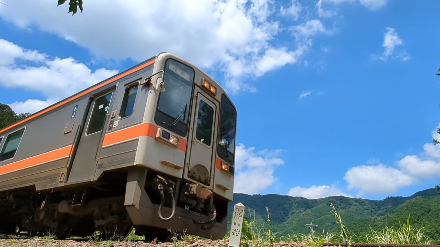 Train with orange stripes under a blue sky and mountains