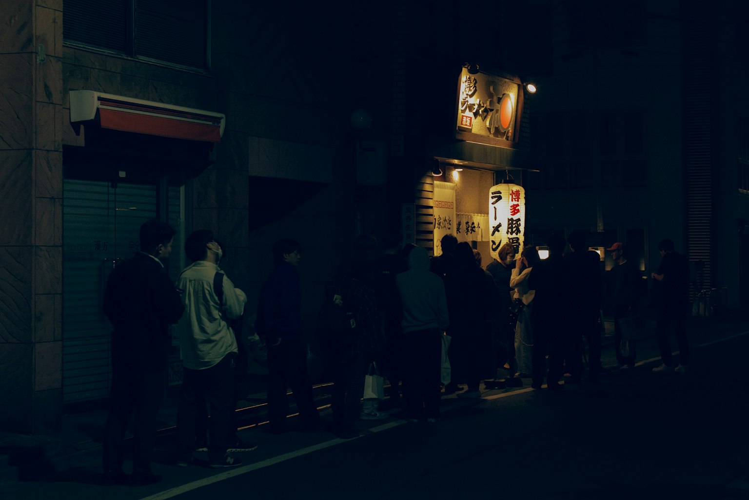 Persone in fila su una strada buia davanti a un negozio illuminato