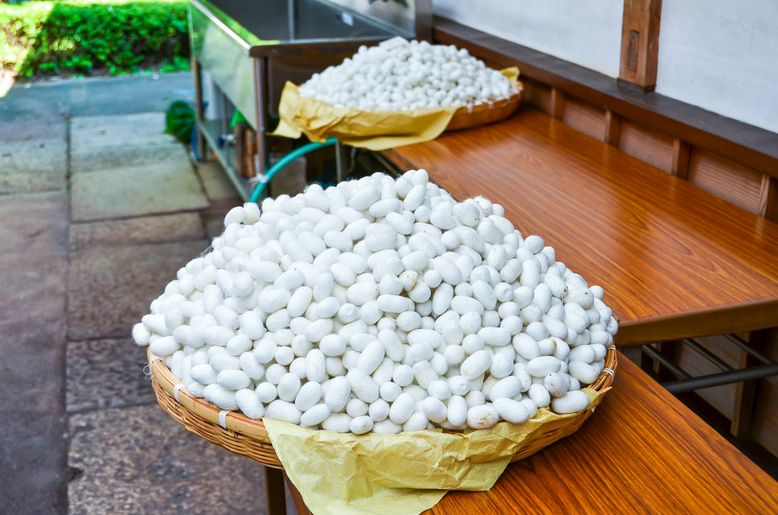 Zwei Körbe mit weißen Seidenkokons auf Holztischen