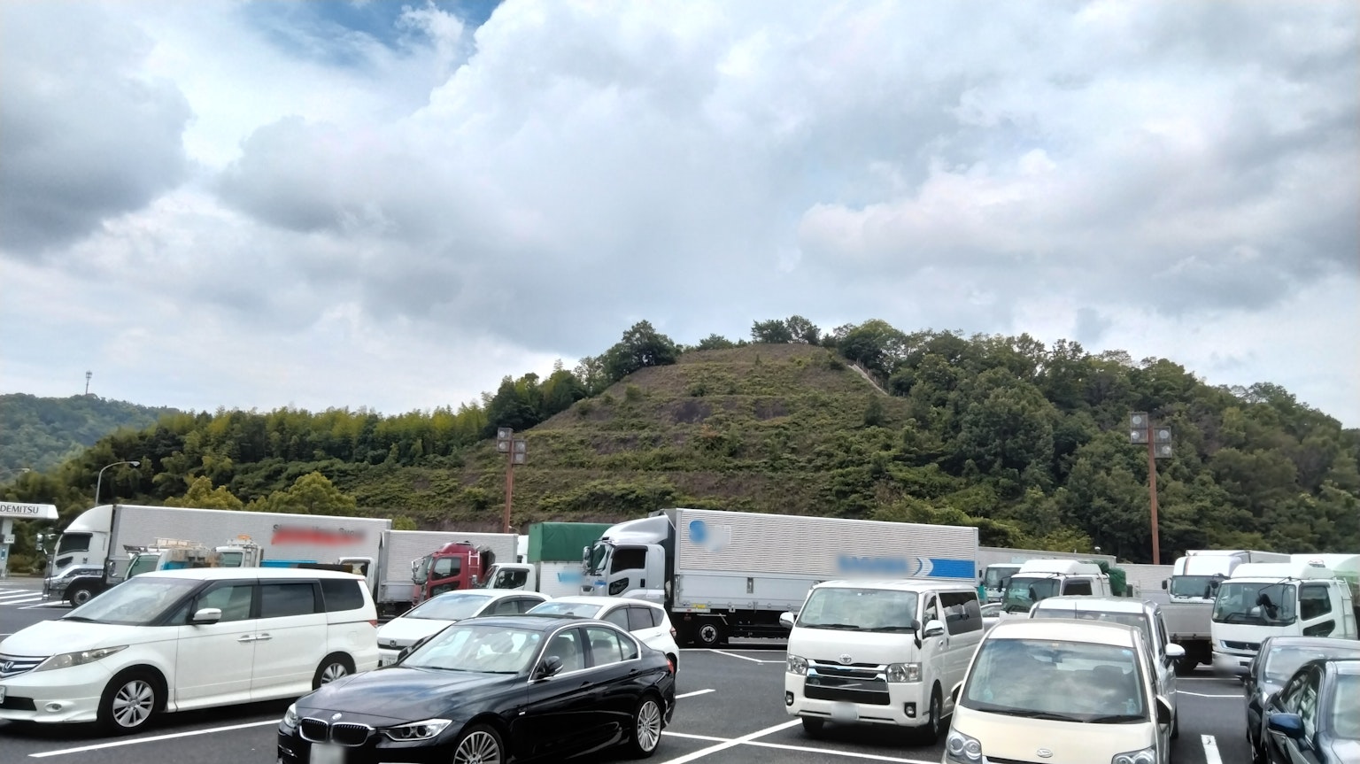 Muchas coches estacionados en un aparcamiento con una colina al fondo