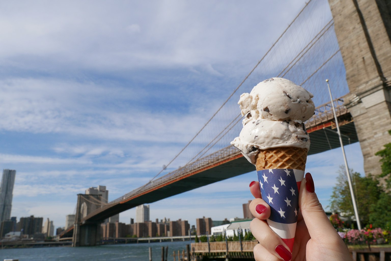 Hand, die eine Eistüte mit der Brooklyn Bridge im Hintergrund hält
