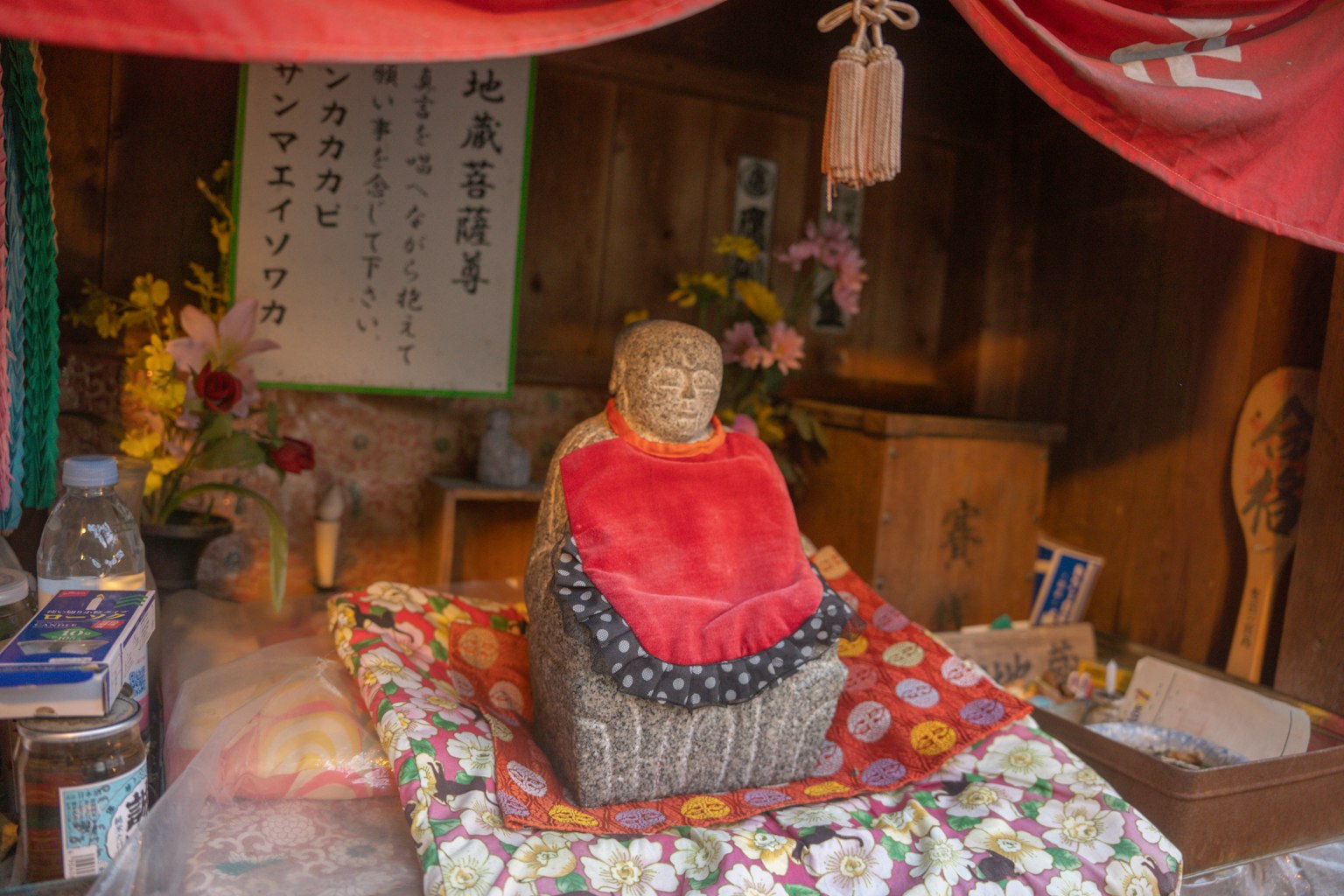 Un piccolo santuario con una statua di Buddha coperta circondata da fiori e offerte