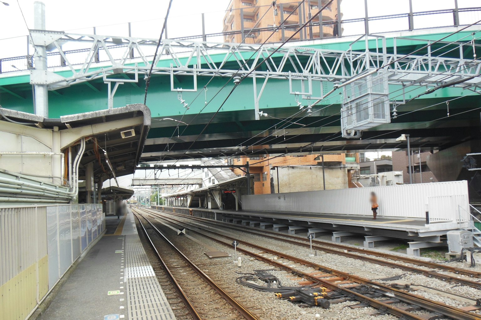 Pemandangan platform stasiun kereta dan rel dengan jembatan tinggi berwarna hijau