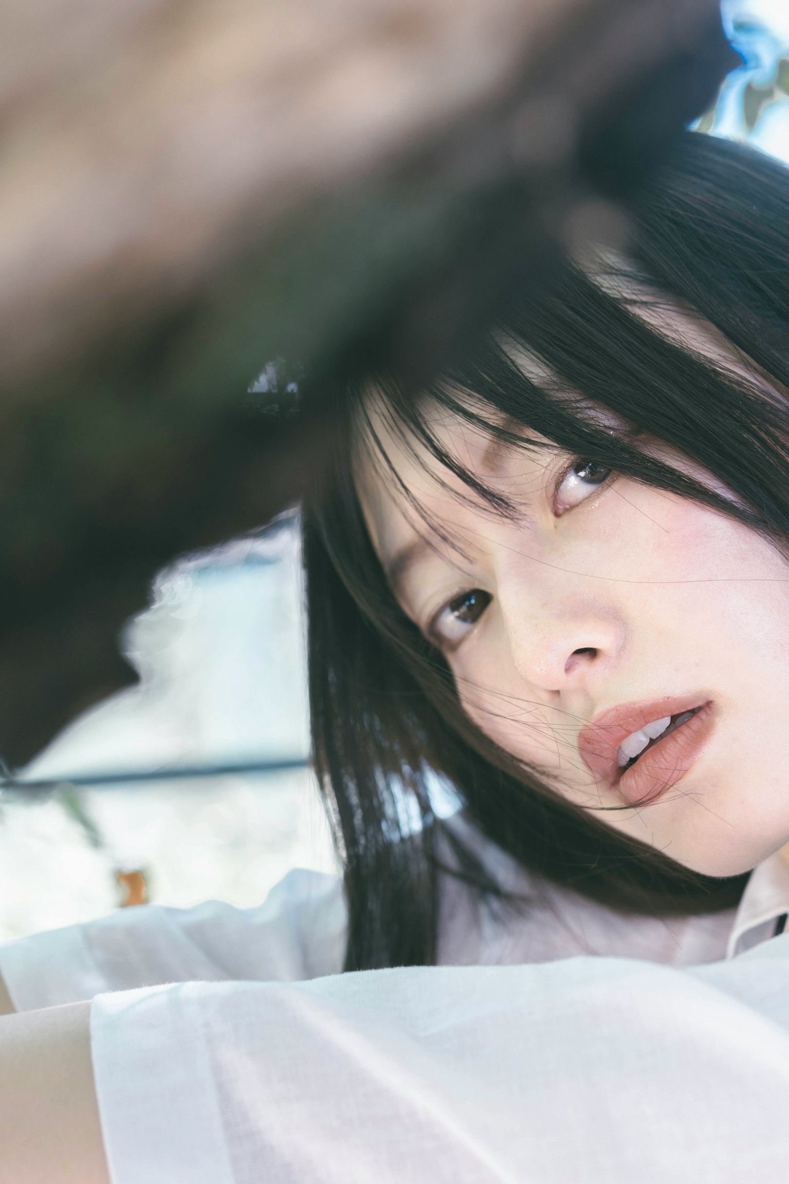 Close-up of a young woman's profile partially obscured by tree branches