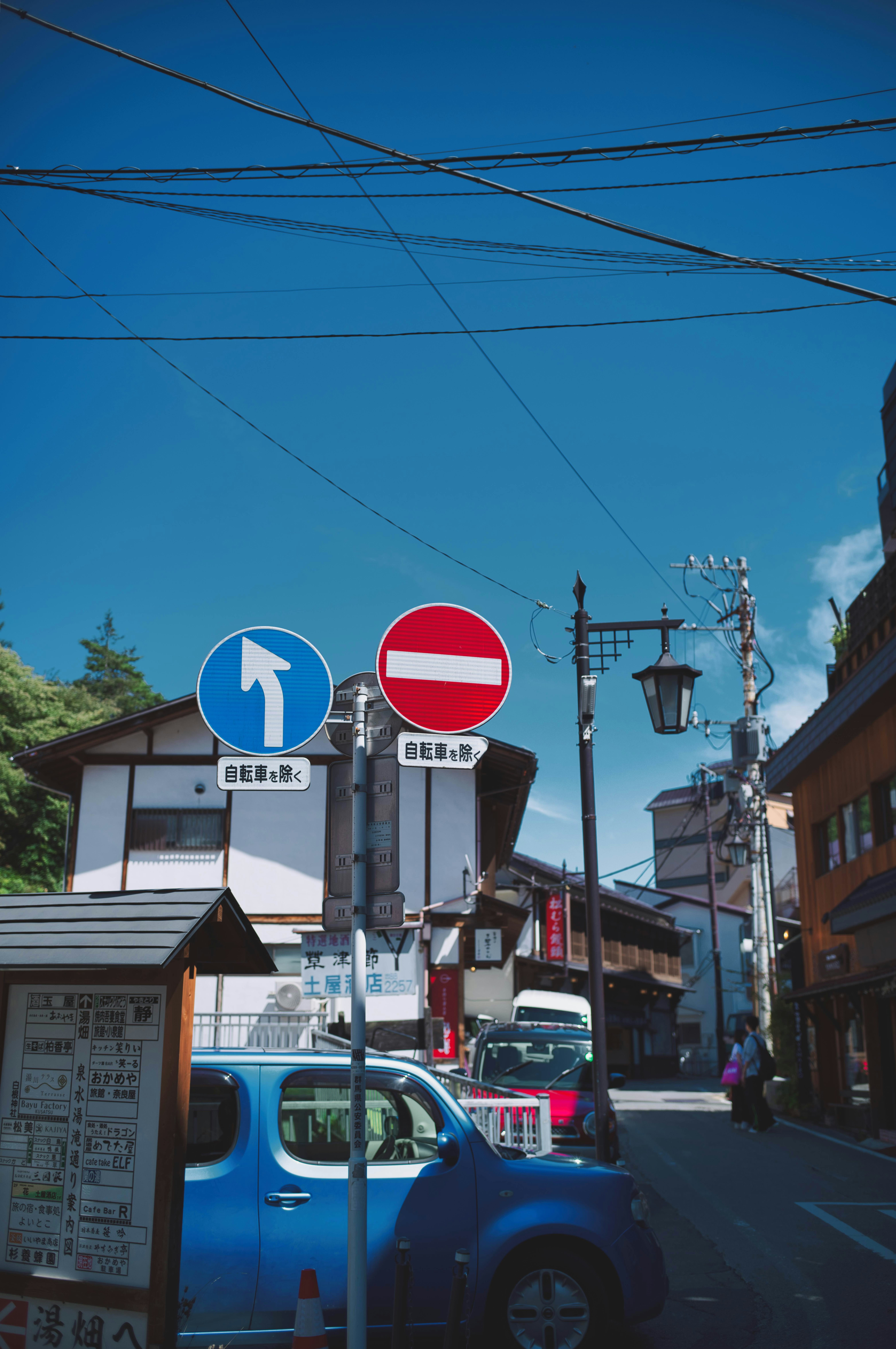青空の下の路地に並ぶ看板と車