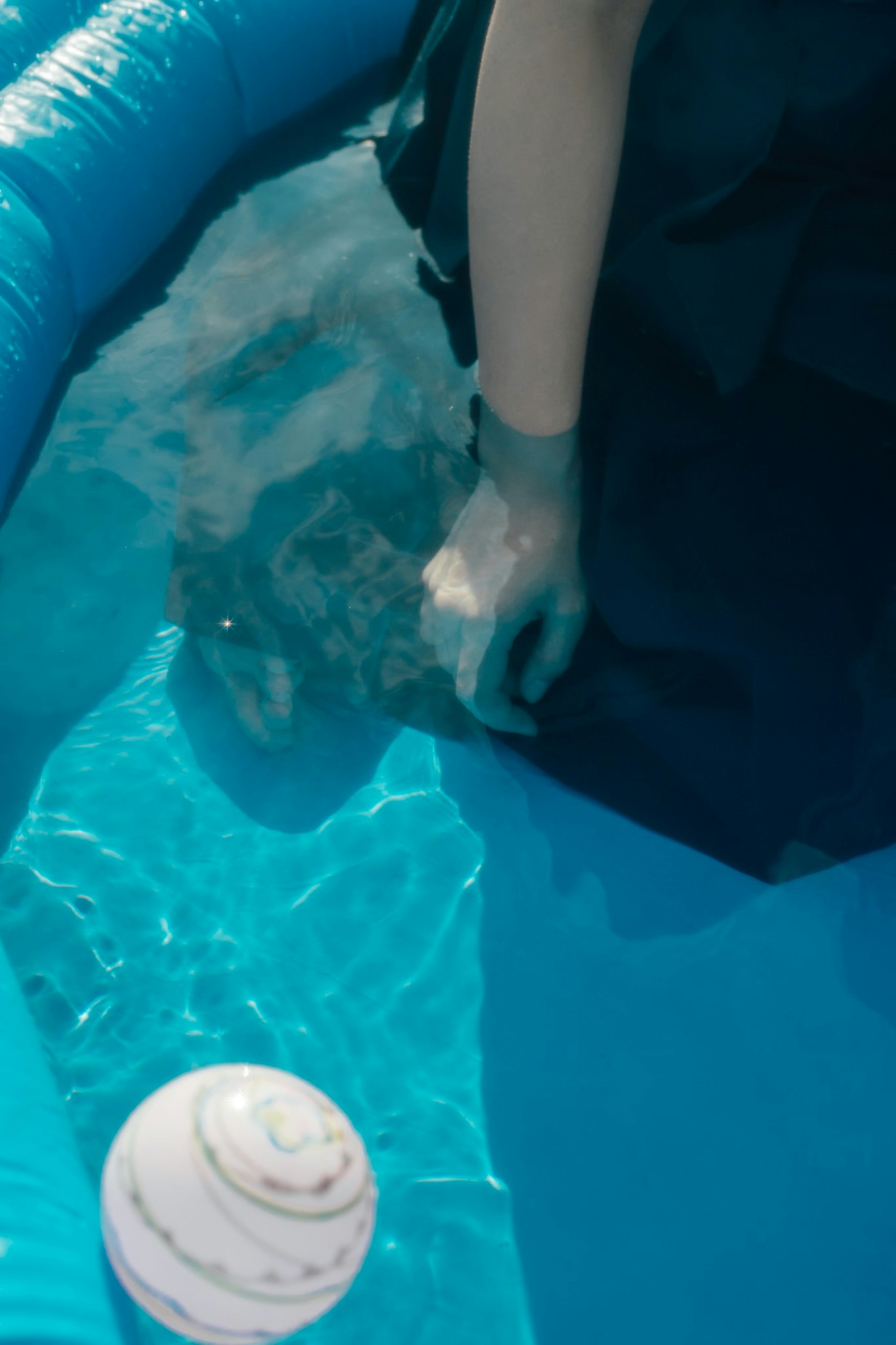 水中のプールで浮かぶおもちゃと人の脚のある光景
