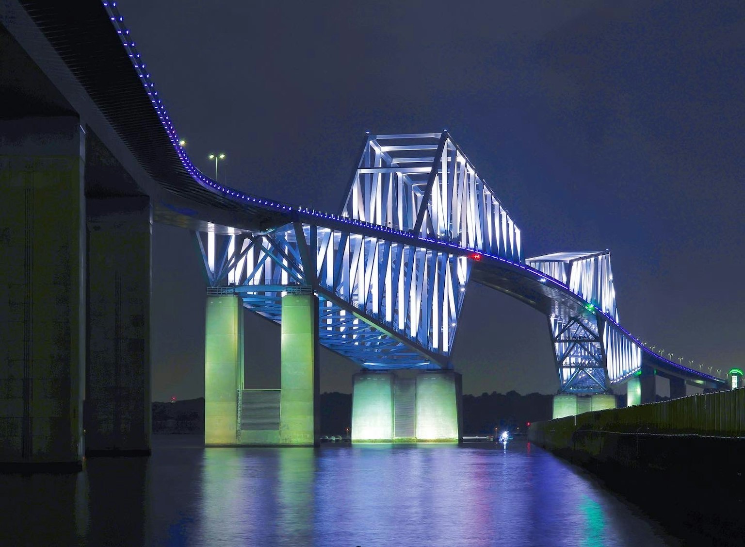 Pont illuminé par des lumières bleues la nuit se reflétant sur l'eau