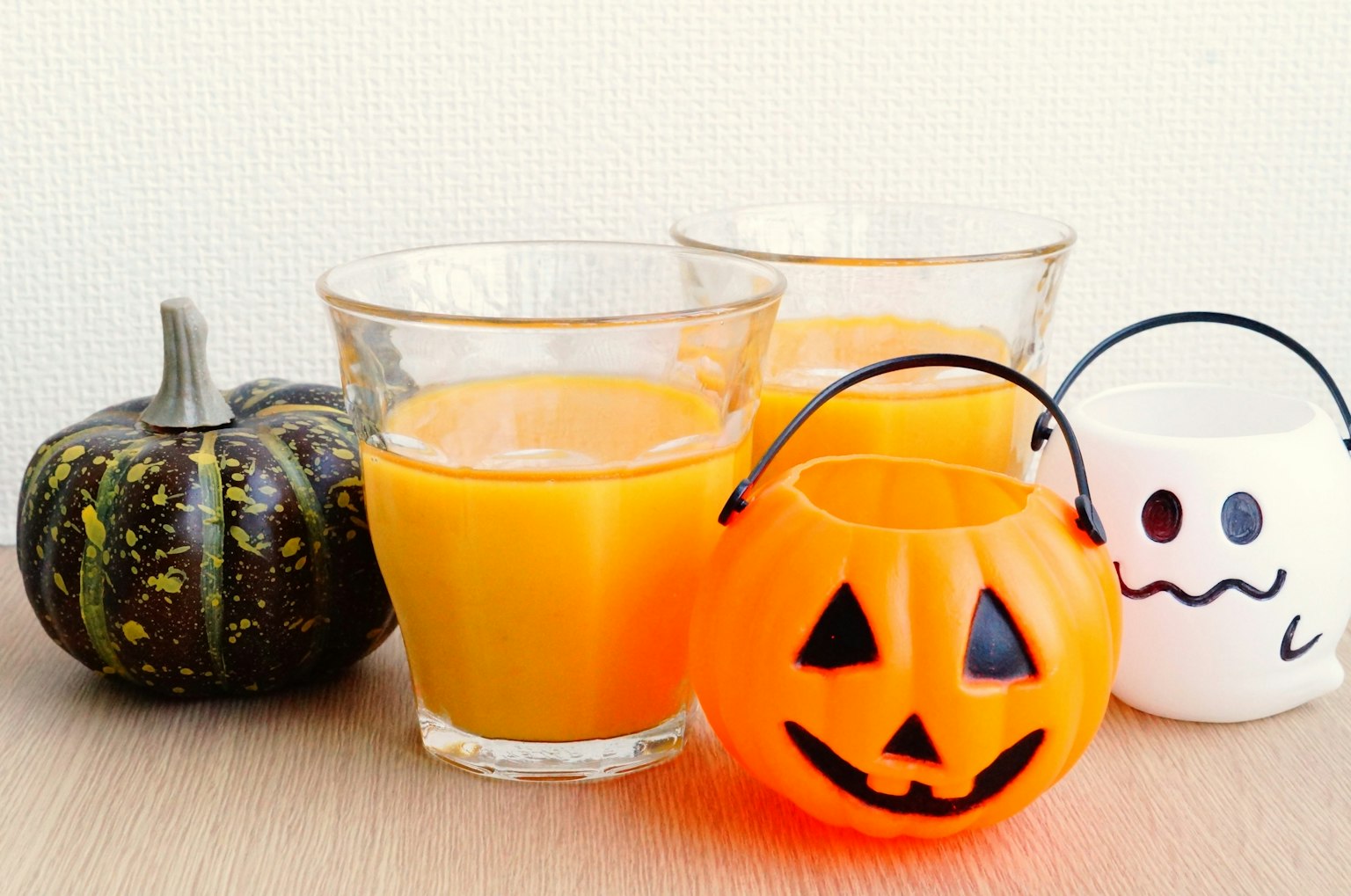 Bebidas naranjas de Halloween en vasos con un cubo de caramelos en forma de calabaza y una decoración de fantasma blanco