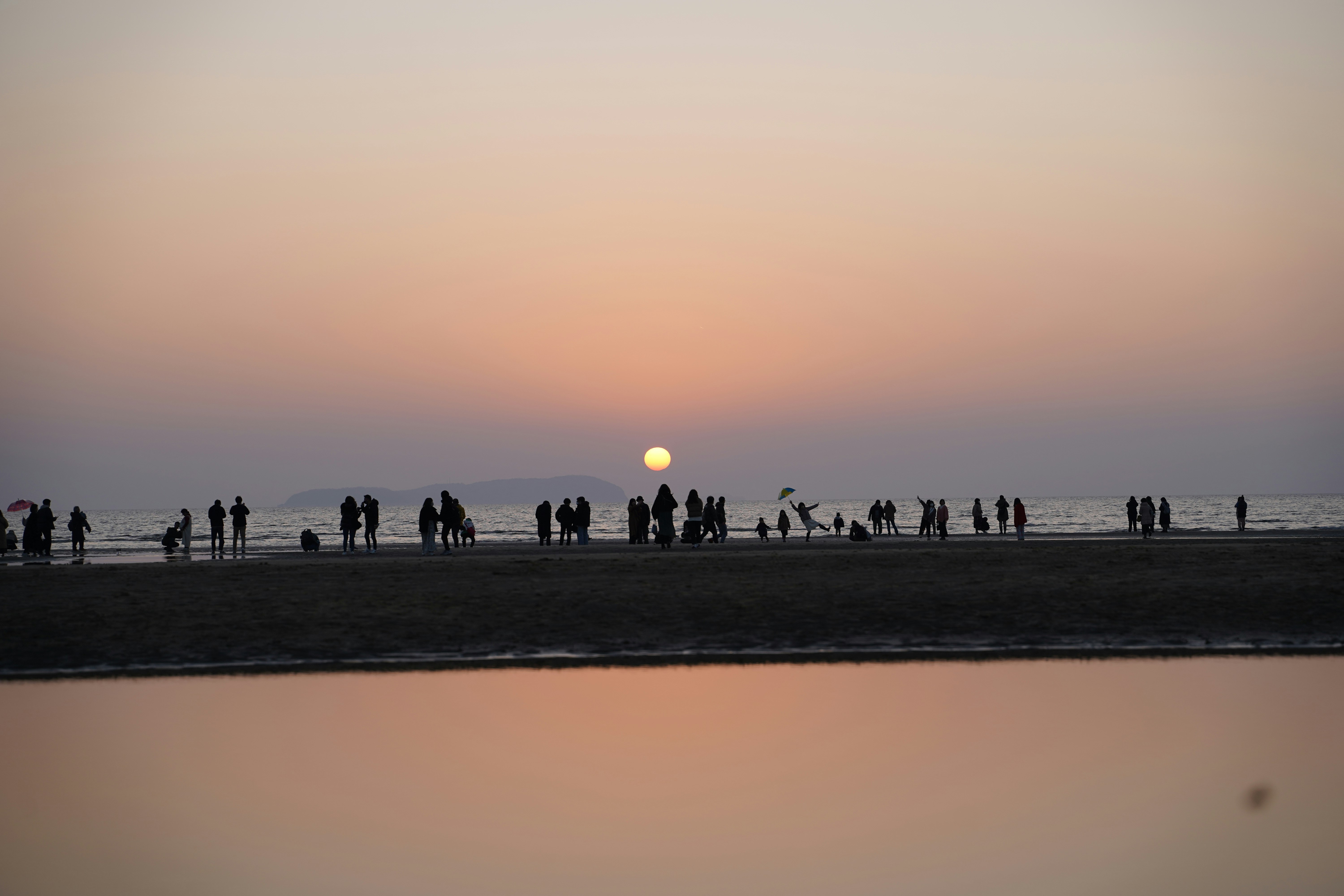 夕暮れの海辺で人々が散歩する砂浜