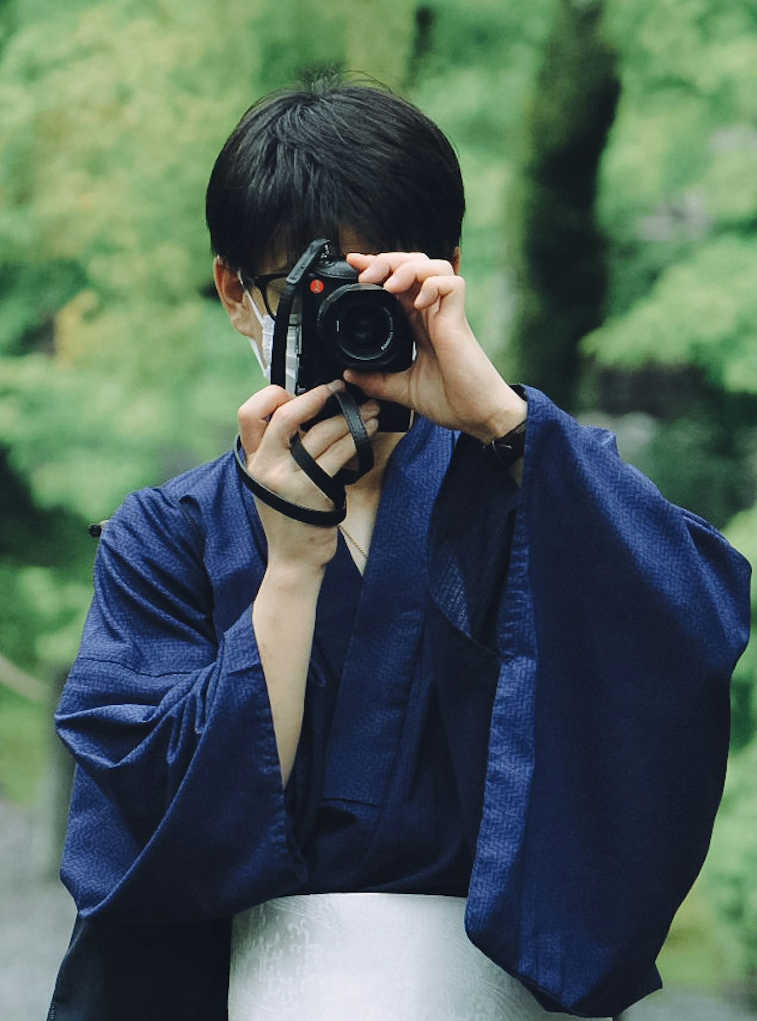 Persona en kimono azul sosteniendo una cámara frente a un fondo verde