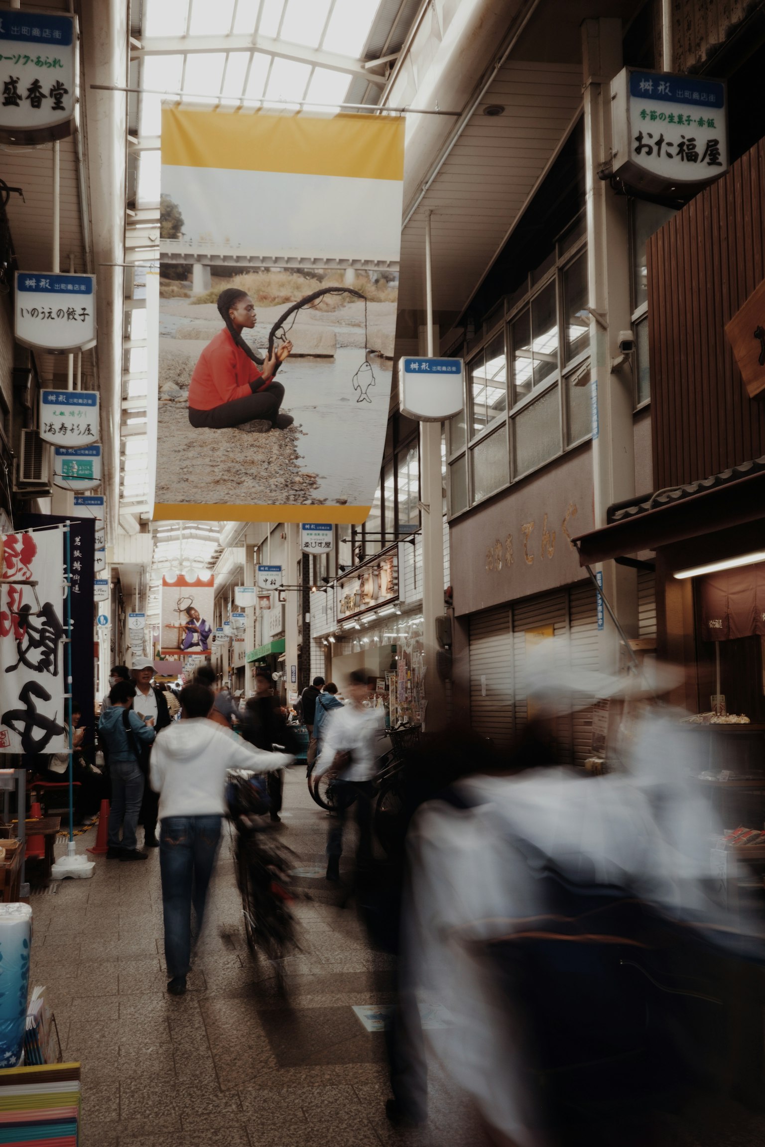 A bustling shopping street with a large banner featuring a person fishing in the background