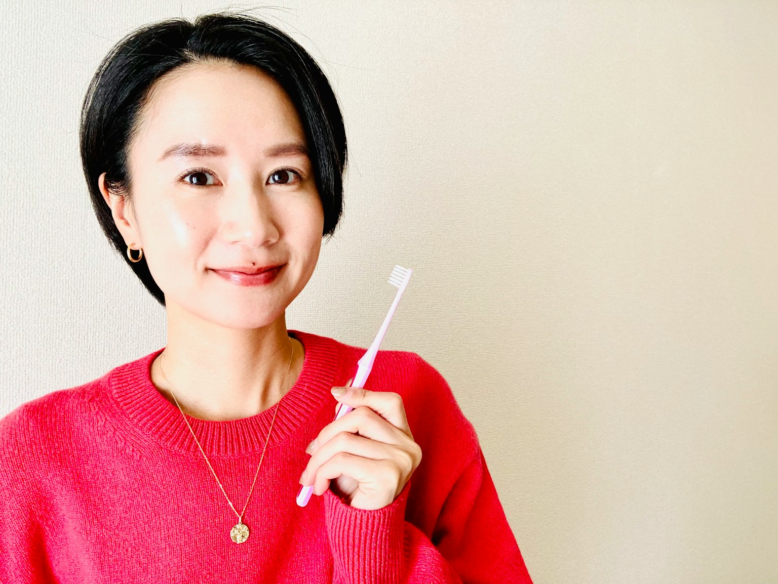 Một người phụ nữ trong áo len hồng cầm bàn chải đánh răng và mỉm cười