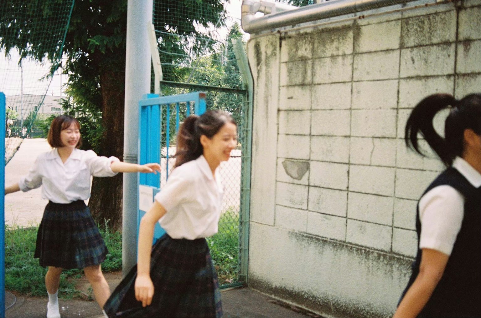 制服を着た女子学生たちが楽しそうに走っている学校の外の風景
